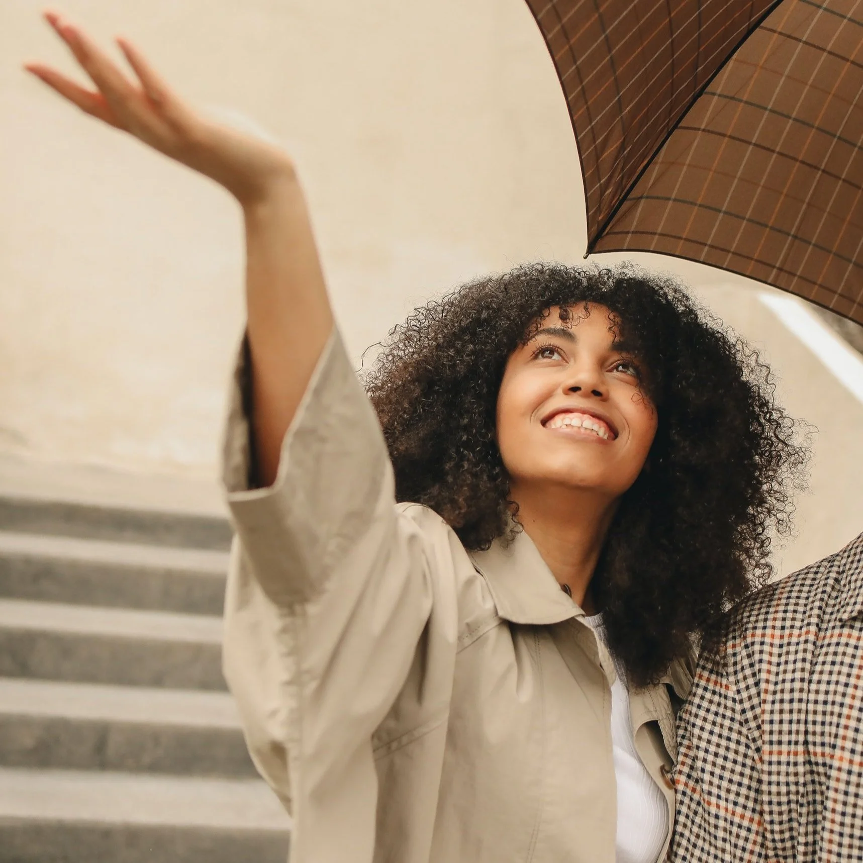 Person smiling with arm extended under an umbrella on a staircase.