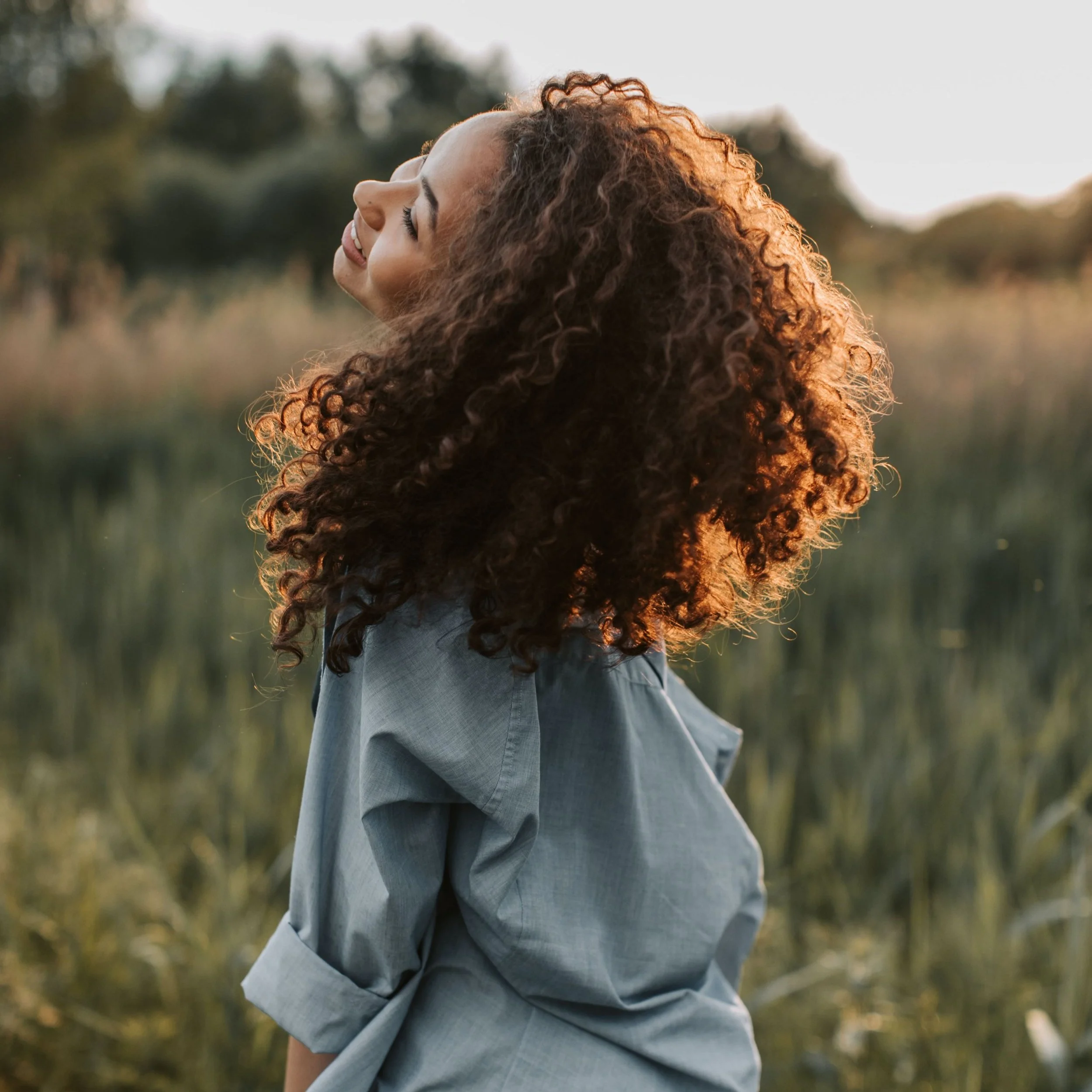 A black woman with curly hair dancing and smiling outdoors