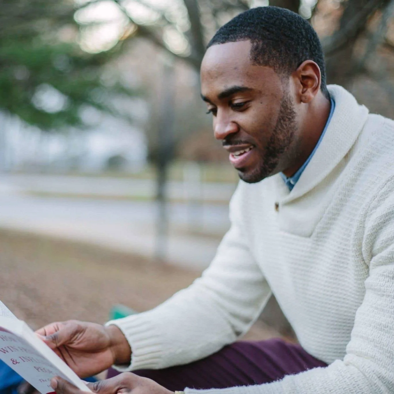A black man reading a book in the park.