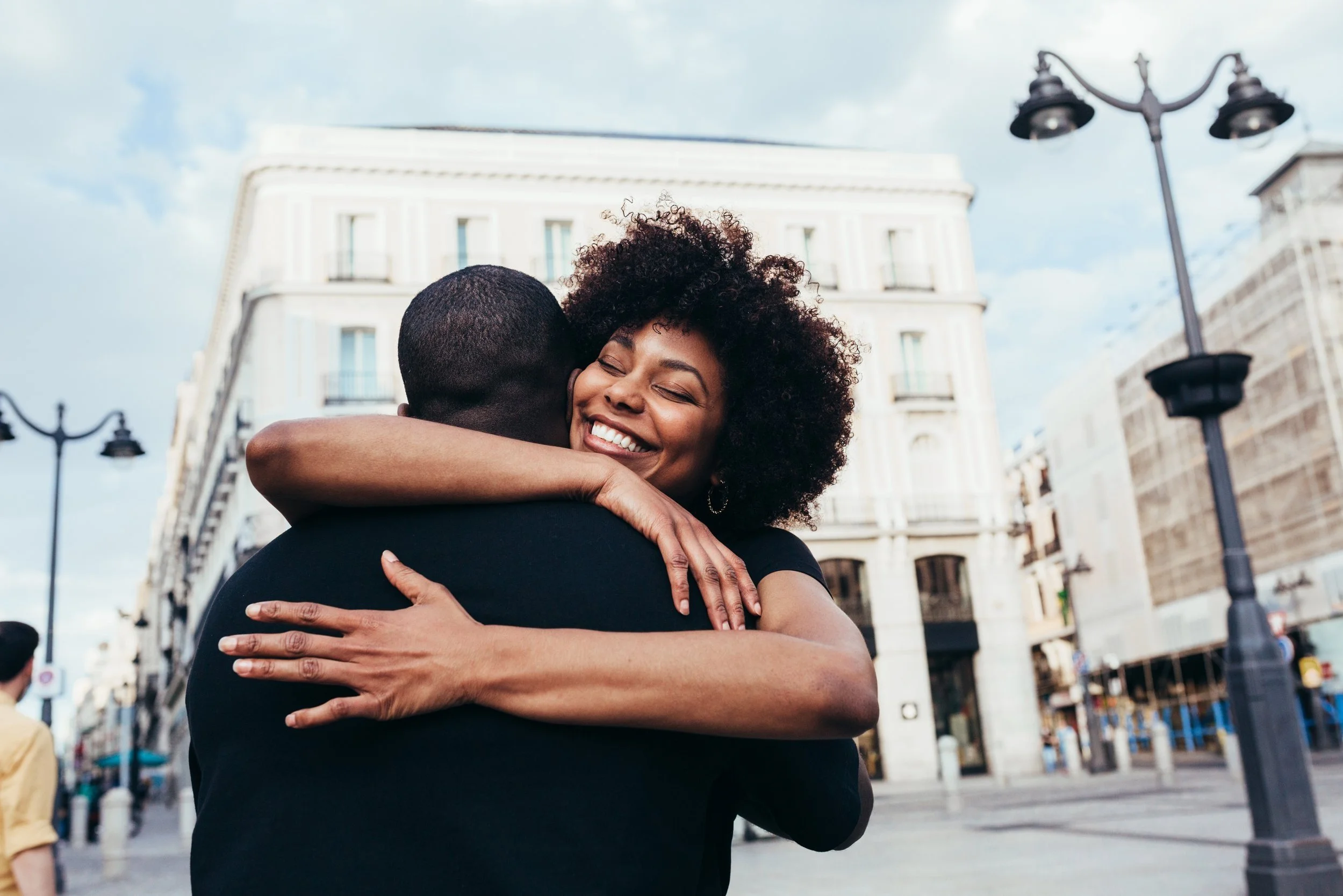 A black woman smiling while hugging a black man