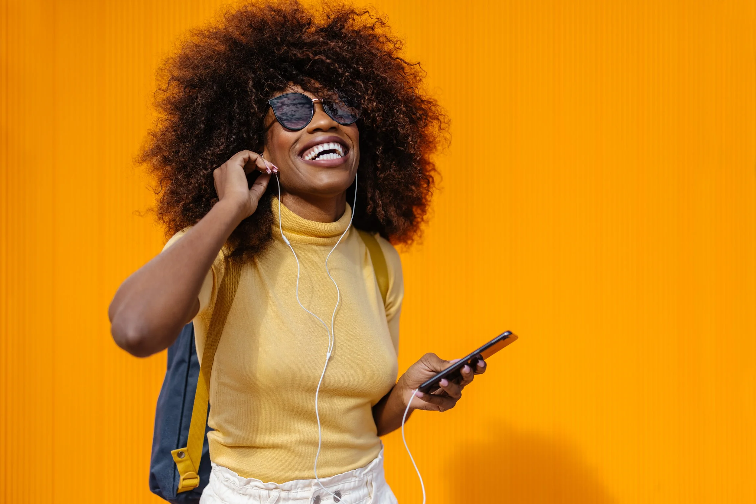 A black woman with a afro smiling while listening to music.