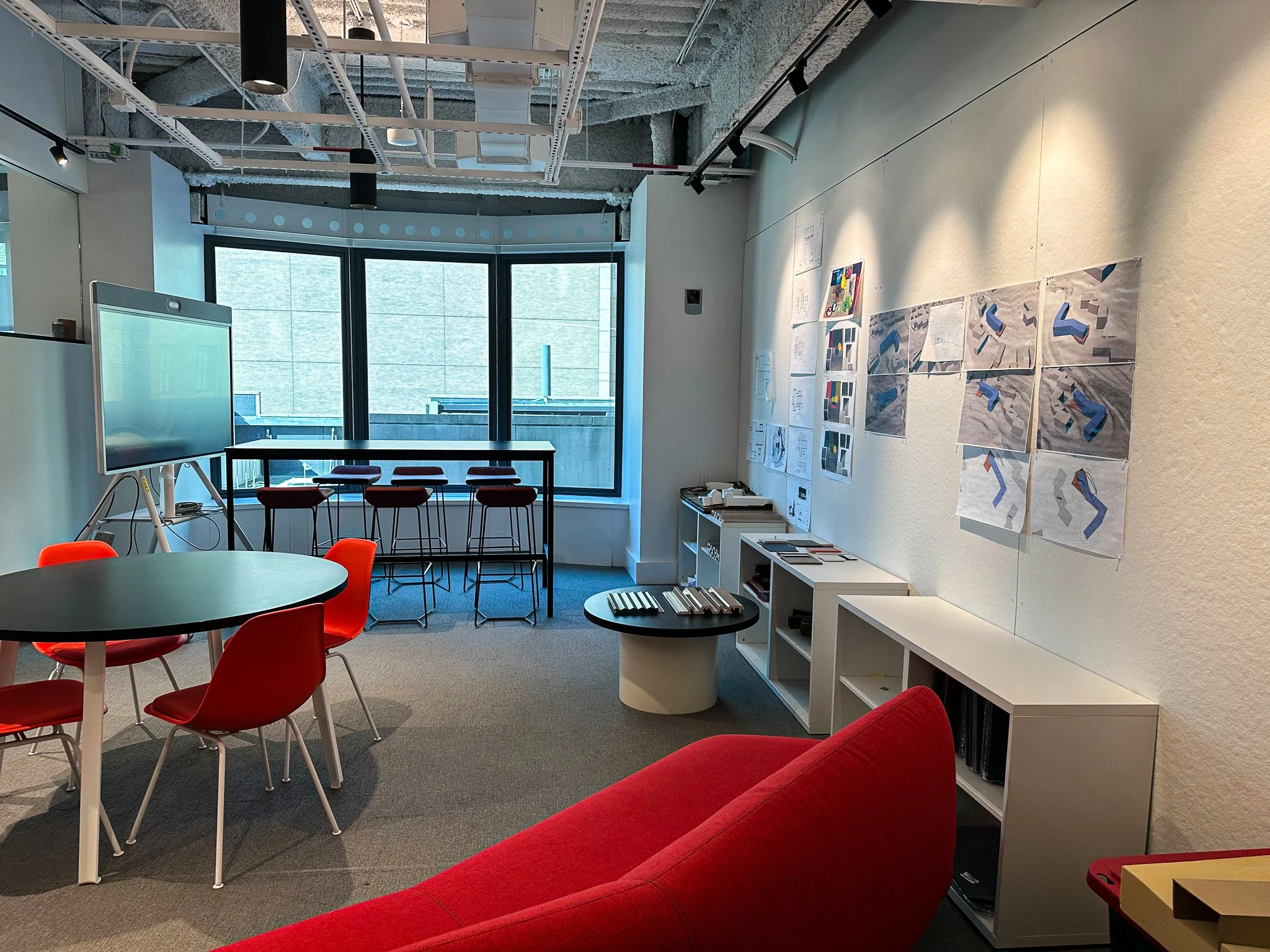 A collaborative space with red chairs and a sofa. There are drawings displayed on the wall to the right.