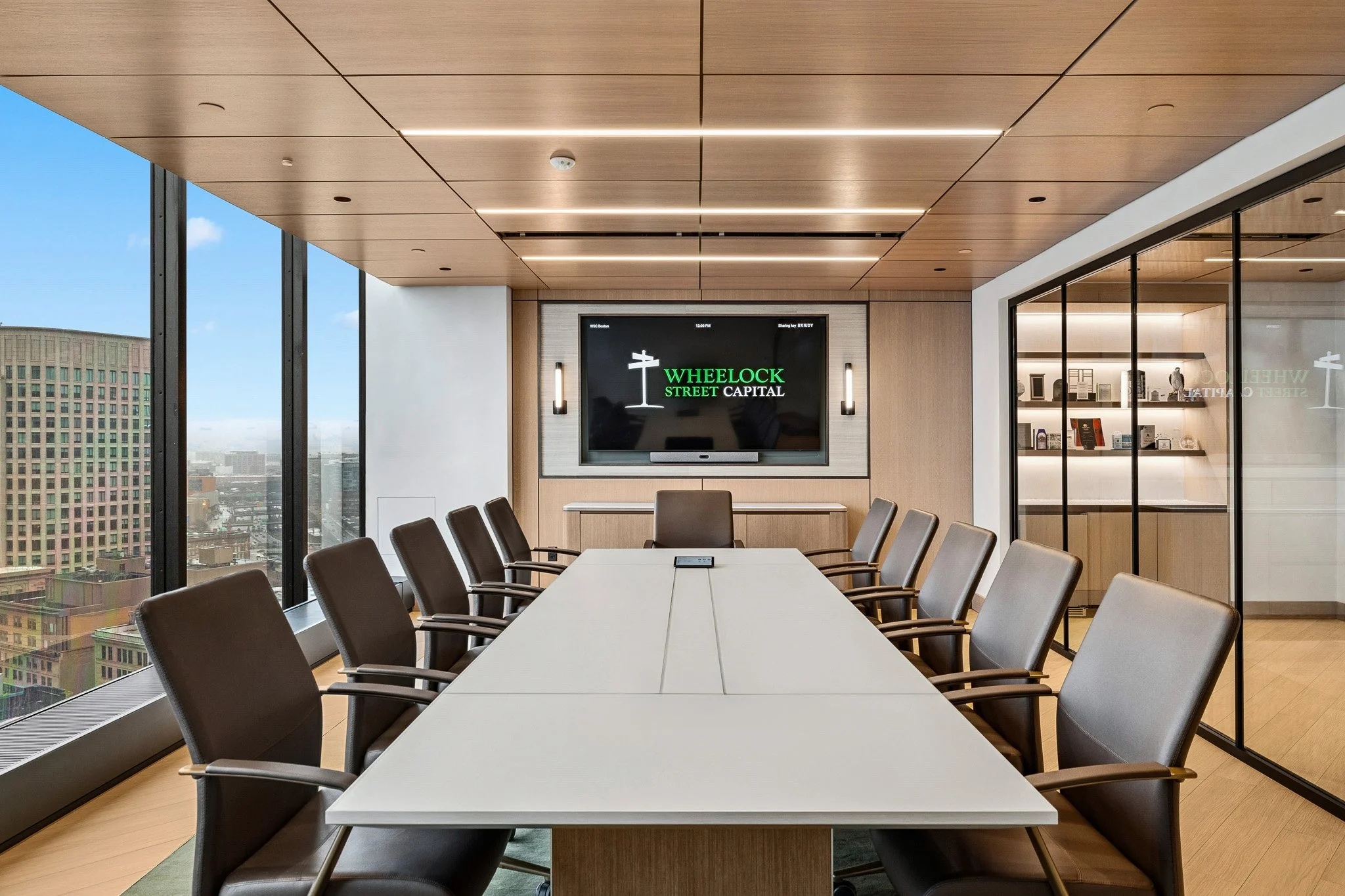high end conference room with millwork ceiling and overhead lighting. there are large floor to ceiling windows that show a view over the Boston skyline.
