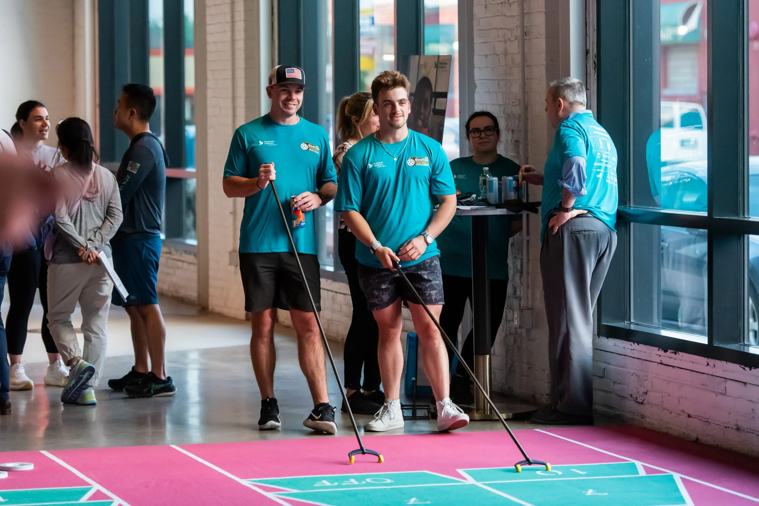 Two Corderman Employees playing shuffleboard at a charity pickle ball event in Boston. Standing next to each other wearing teal shirts