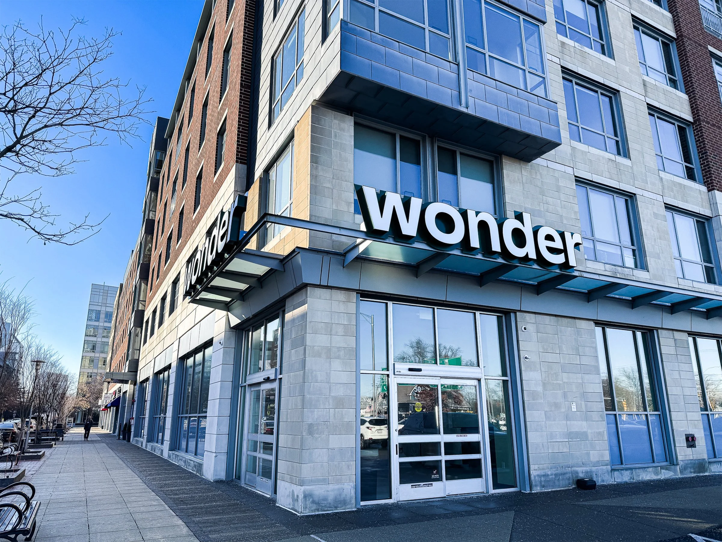 The exterior of a new Wonder location at Station Landing in Medford, MA. Standing at the corner of the building, two Wonder signs are visible on the brick and stone, multi-floor building.