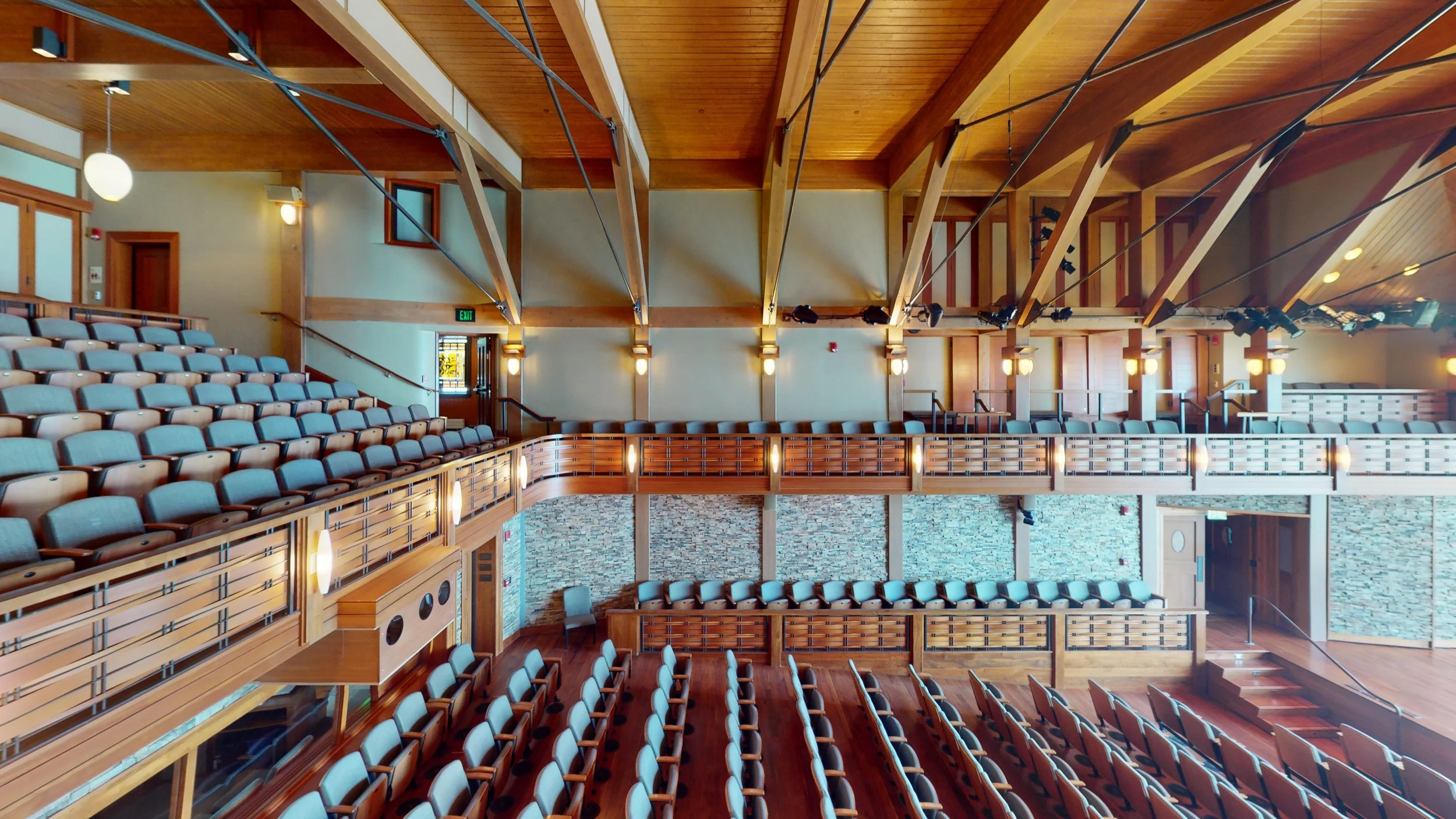 View of the Shalin Liu Performance Center in Rockport, MA. Rows of seating within a stunning event venue, wooden beams overhead, and railings crafted from woven wood create a captivating environment.