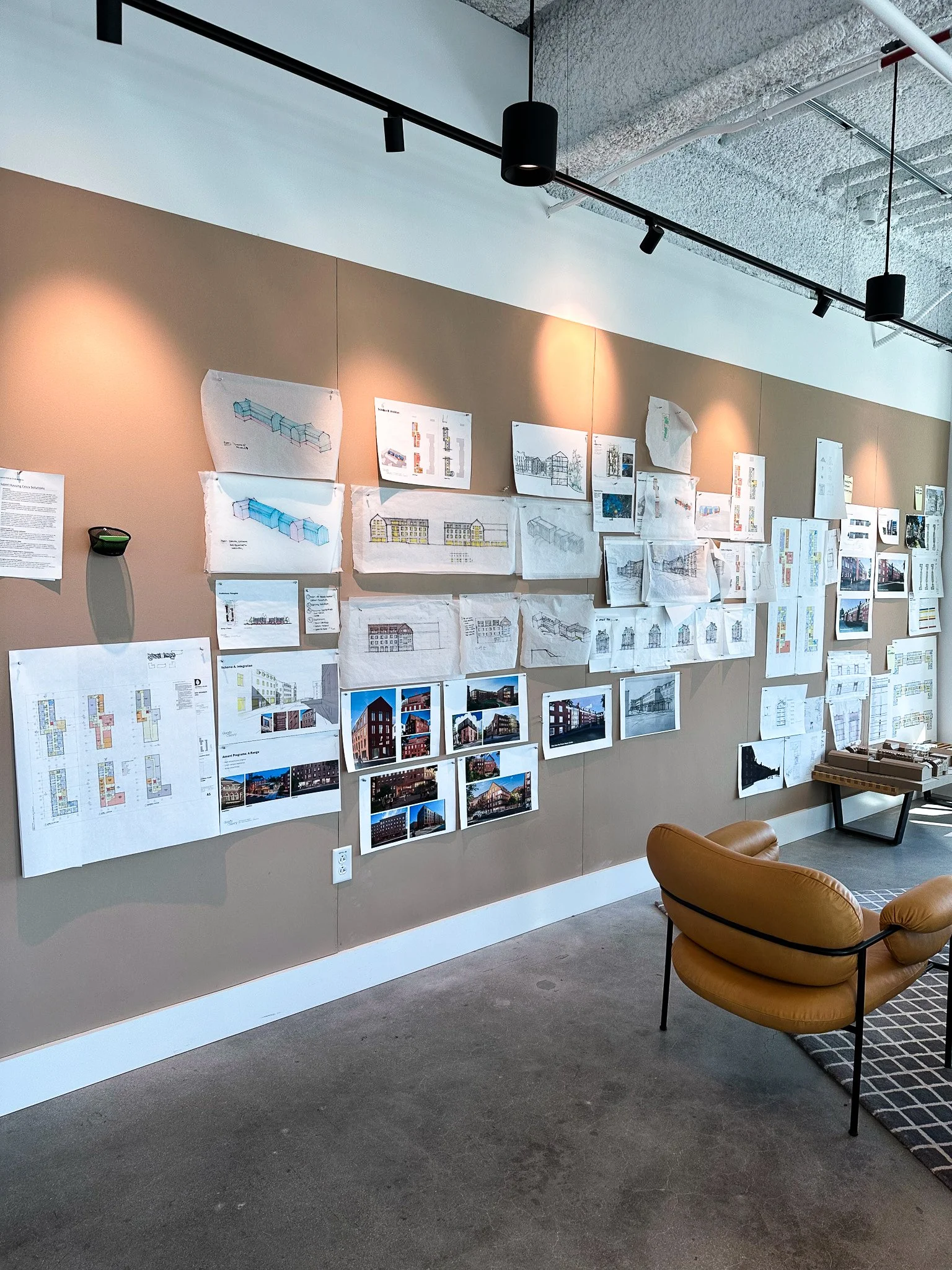 Architectural sketches are pinned up on a wall, with lights gleaming down upon them. They are produced by Goody Clancy, whose new office is located in Downtown Boston at 99 High Street.