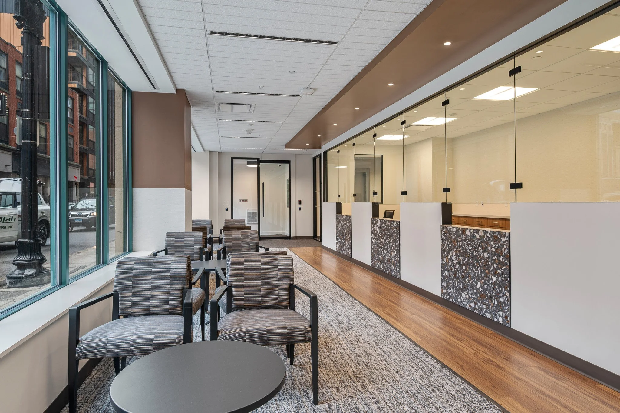 Glass windows line the left side, looking onto Friend Street in the North End. There are seats and tables in the middle, a carpet underneath, and a reception area along the right side.