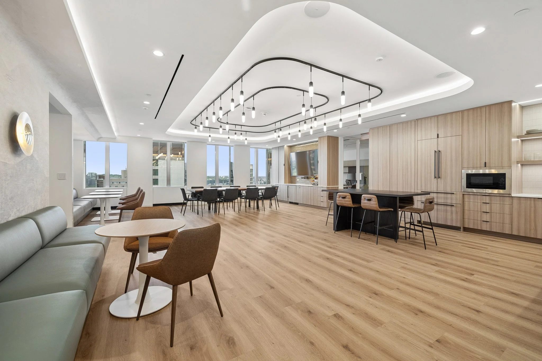 An open seating area at Nonantum Capital Partners. There is a neat lighting fixture in the center of the ceiling, wood floors and cabinetry, and a variety of seating and tables. The space is located at 800 Boylston Street in Boston, MA.
