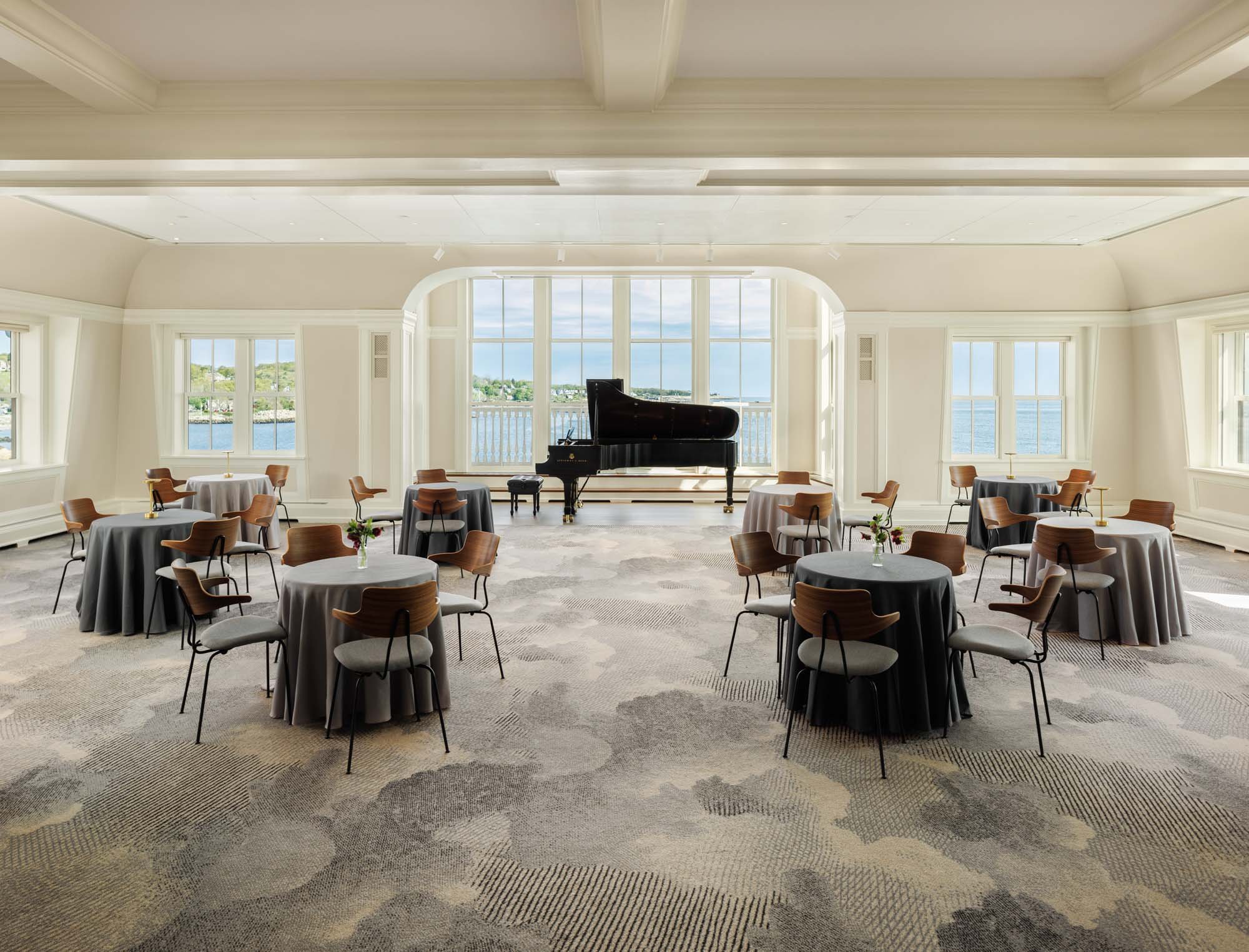 Shalin Liu Performance Center's reception hall. Round tables with chairs are set throughout the space, a Steinway & Sons piano sits in front of large windows that boast a stunning view of the North Shore coastline.