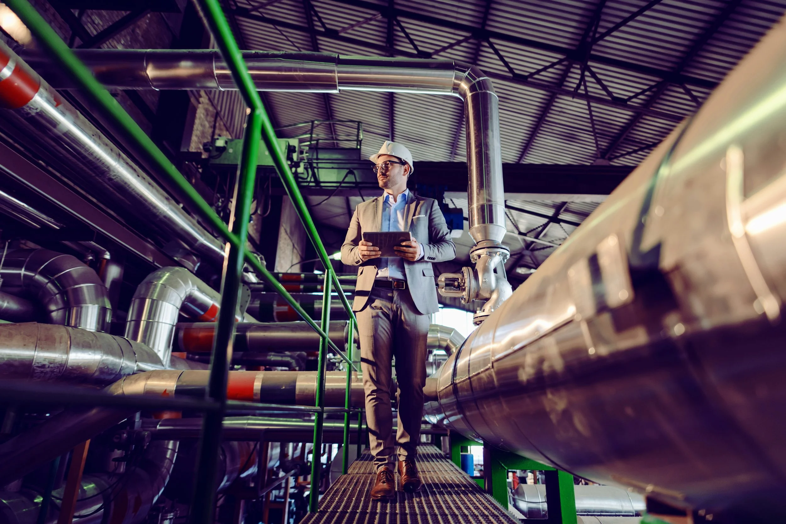 Engineer walking through an industrial mechanical room with exposed piping and equipment.