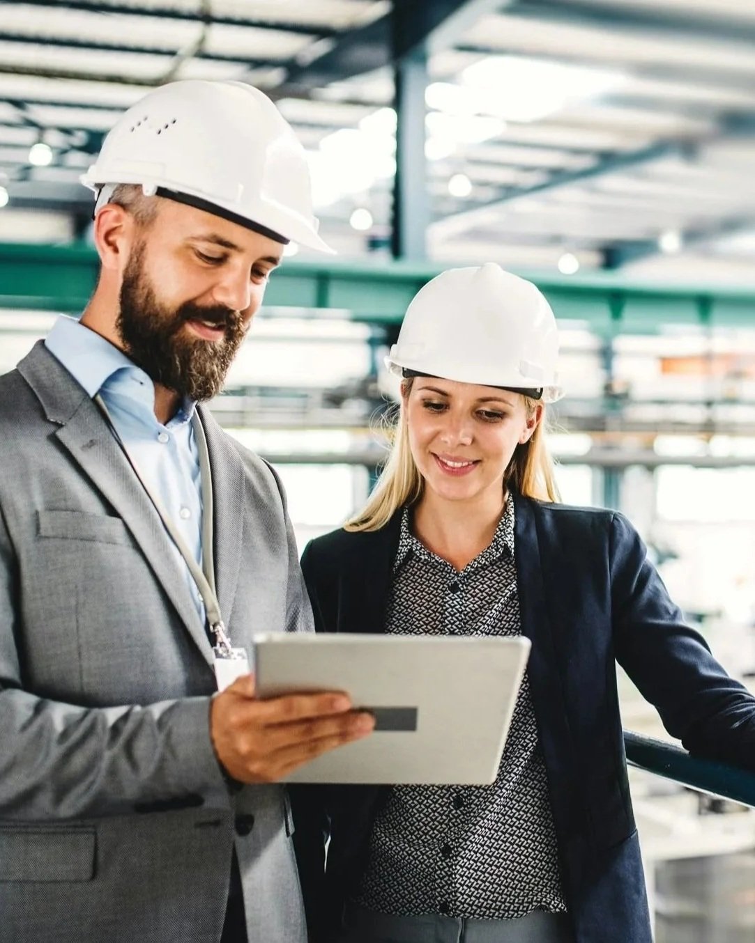 Two engineers wearing hard hats reviewing data on a tablet inside an industrial facility.