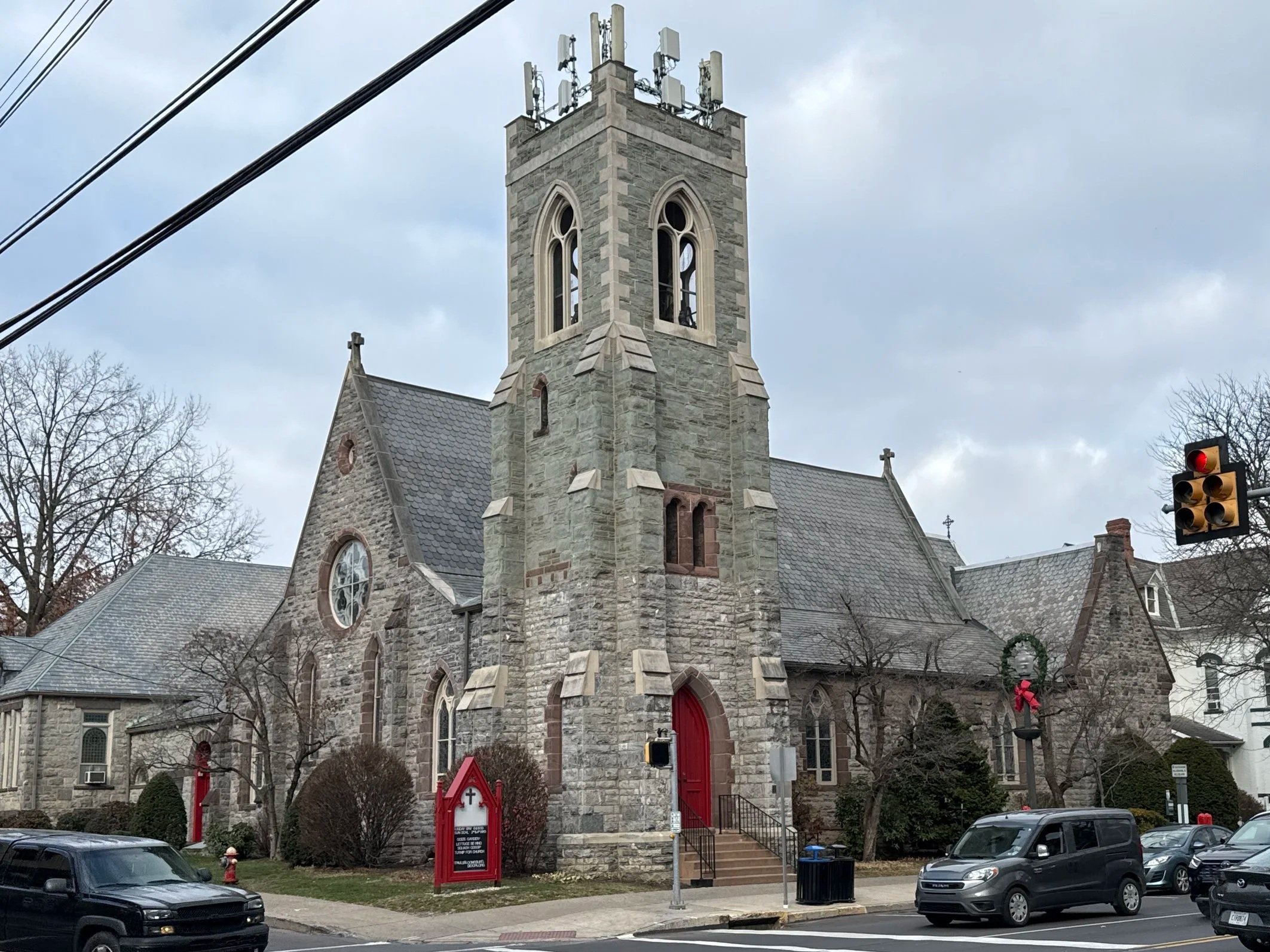 Stone church building with a central tower and arched windows, located at a street corner in a residential neighborhood.