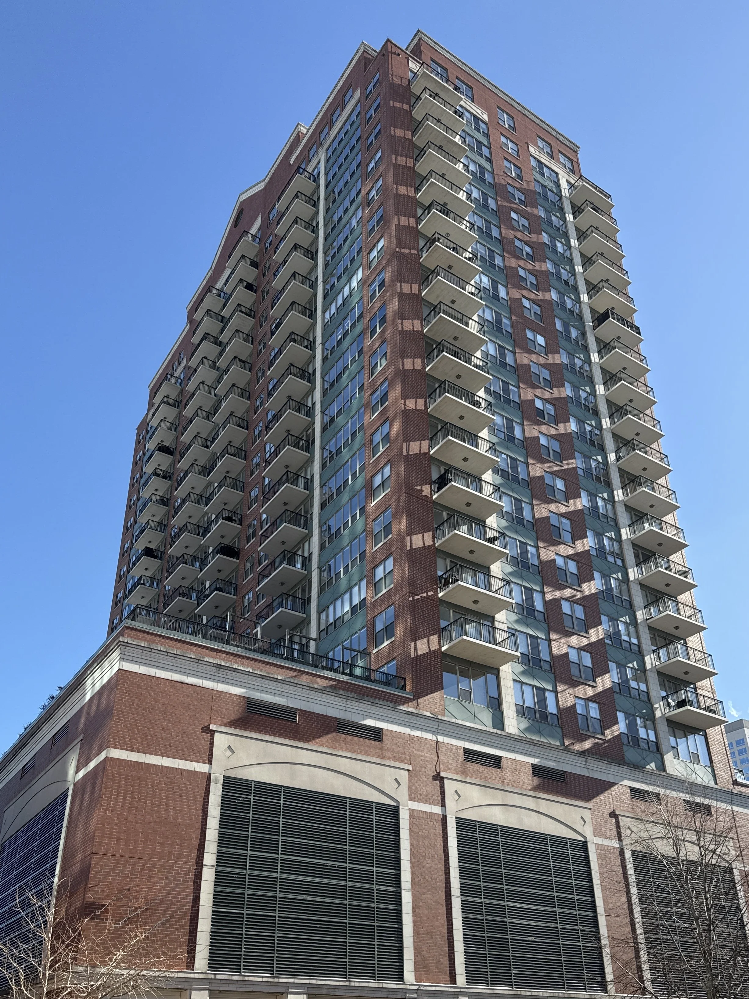 High-rise multifamily residential building with a brick and glass facade, photographed from street level on a clear day.