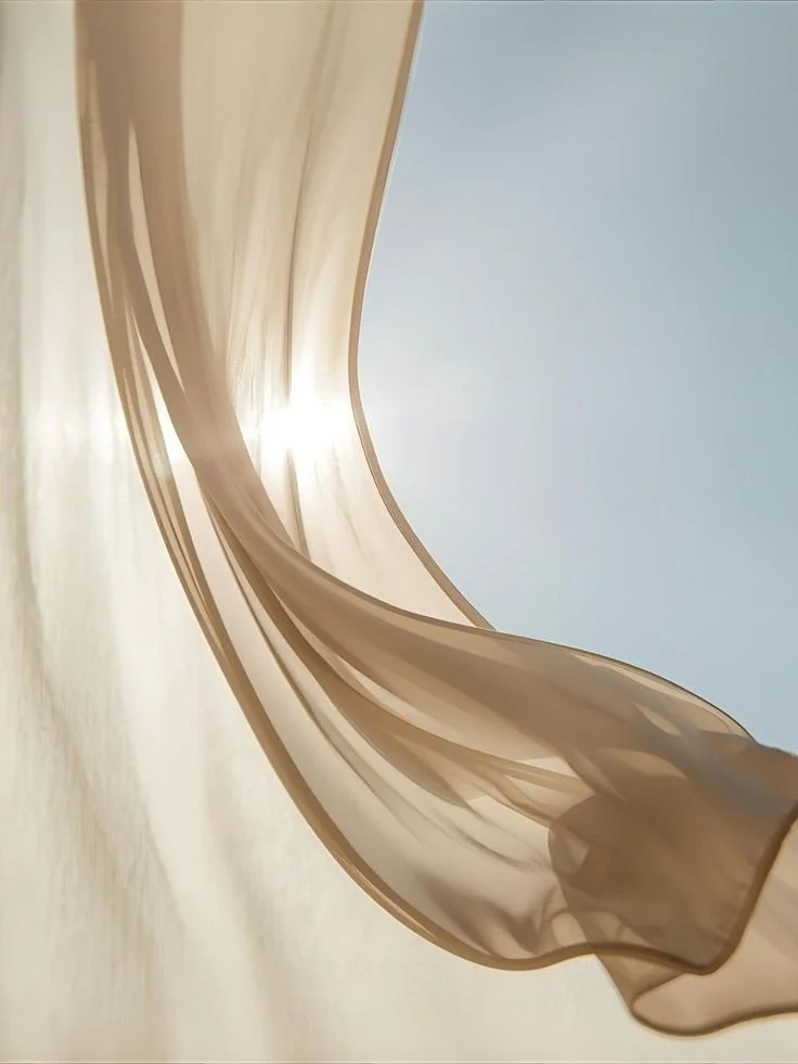 Close-up of a flowing sheer fabric curtain with sunlight filtering through, against a bright sky.