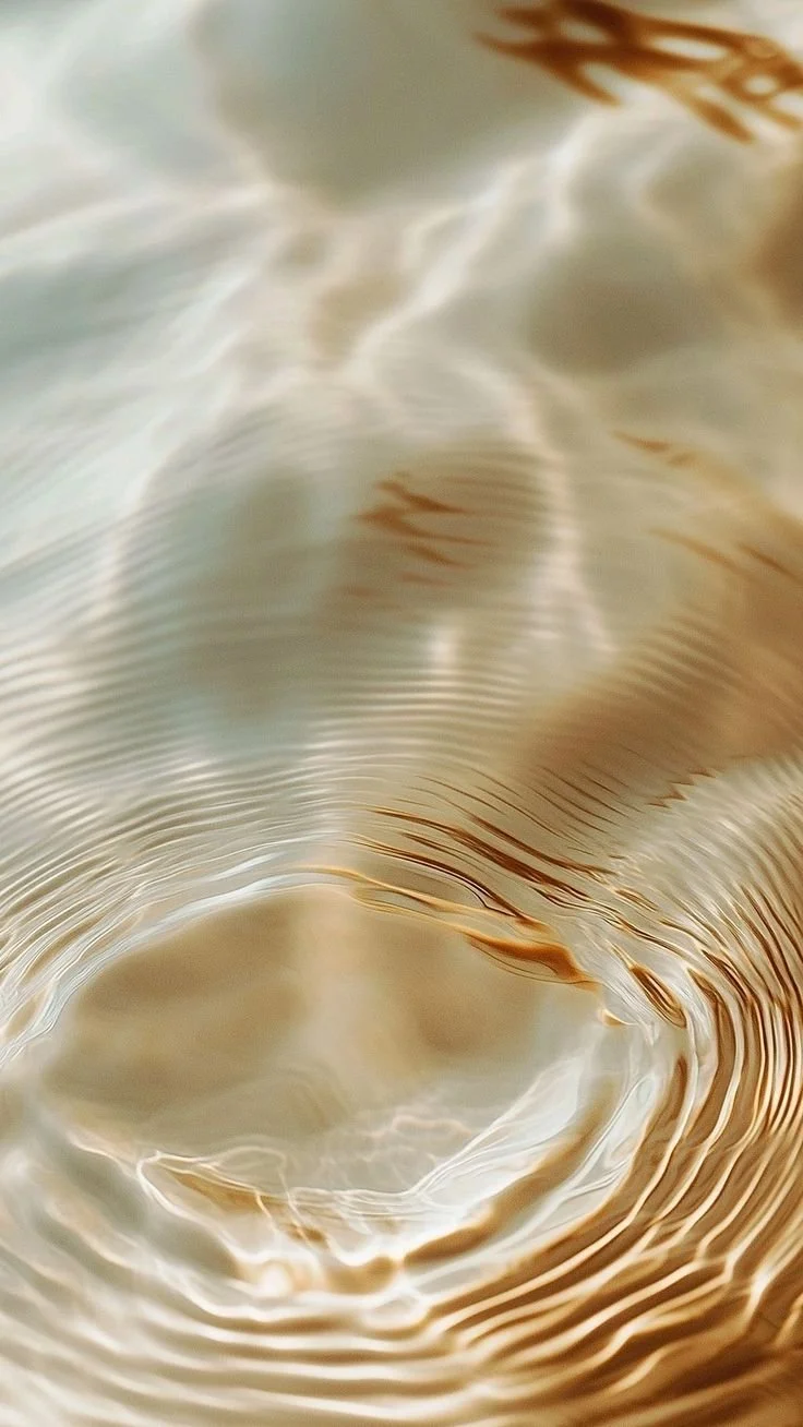 Close-up of the surface of a swirling, golden-colored liquid with ripples and reflections.