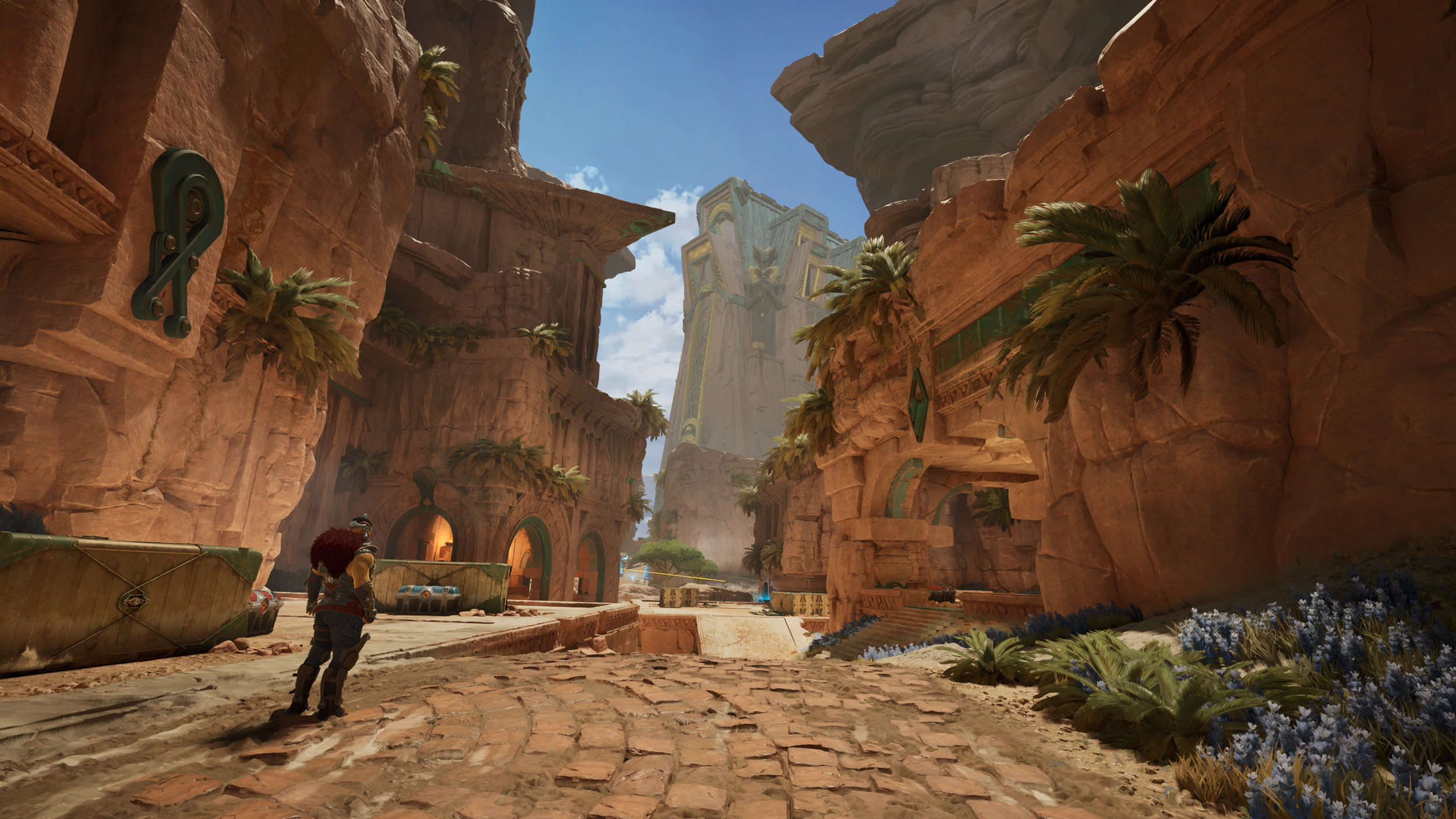 A character with red hair and futuristic armor stands in a desert canyon with tall, reddish rock formations and a futuristic city with large towers in the background.
