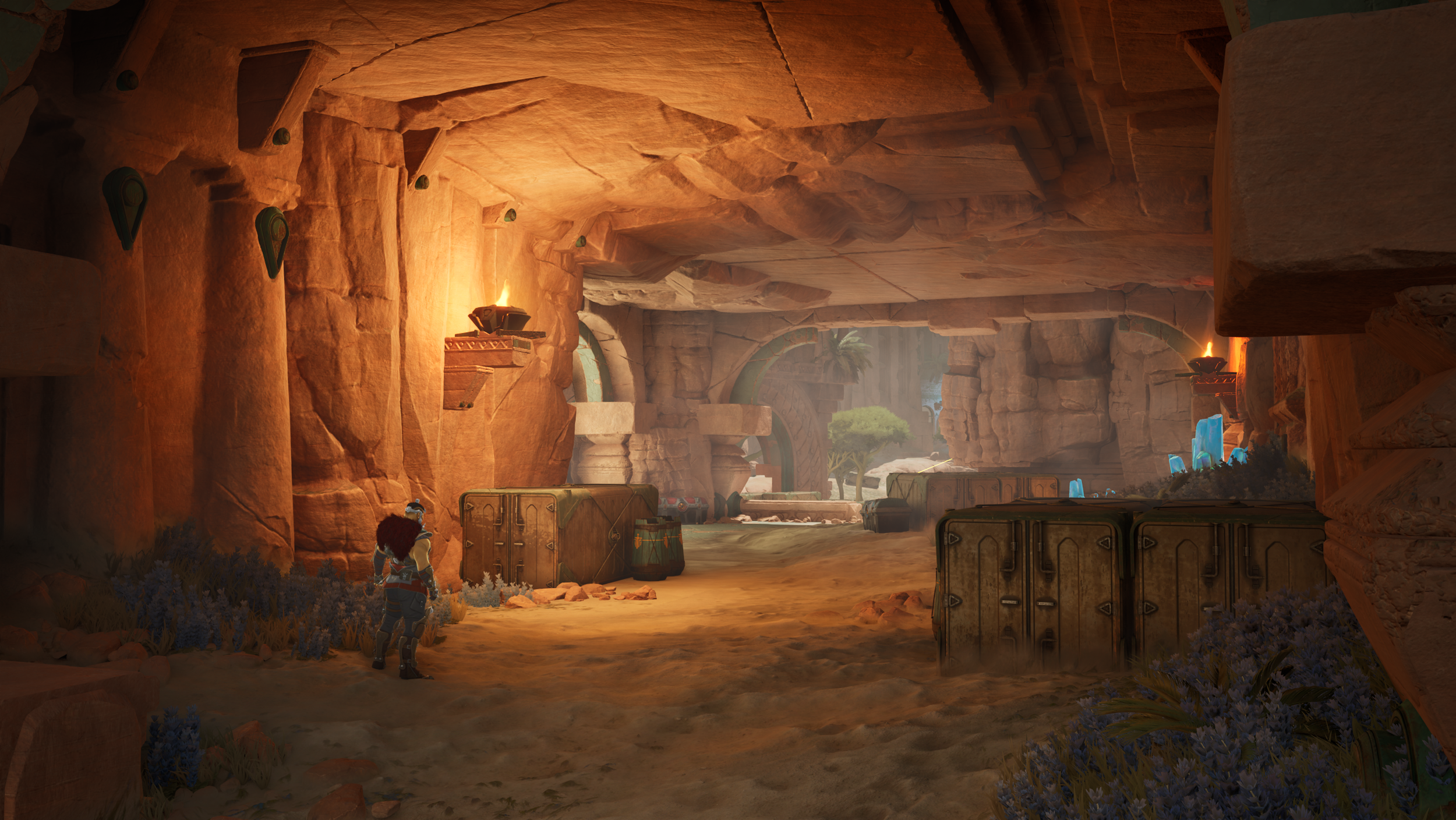 A digital painting of a cave with a futuristic or fantasy style. The cave has orange rock walls and ceiling, with archways leading outside. Inside, there are two characters, one with dark hair and armor, standing near storage containers and plants. T