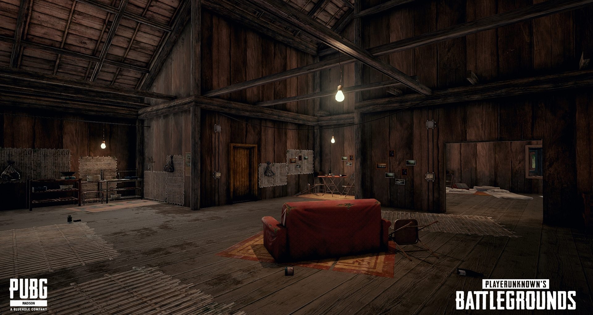 Interior view of a rustic wooden cabin or cabin-like room with a couch, small table, and beds visible. The room has exposed wooden beams, hanging light bulbs, and various pictures or items on the walls. The space appears unfinished or in a state of d