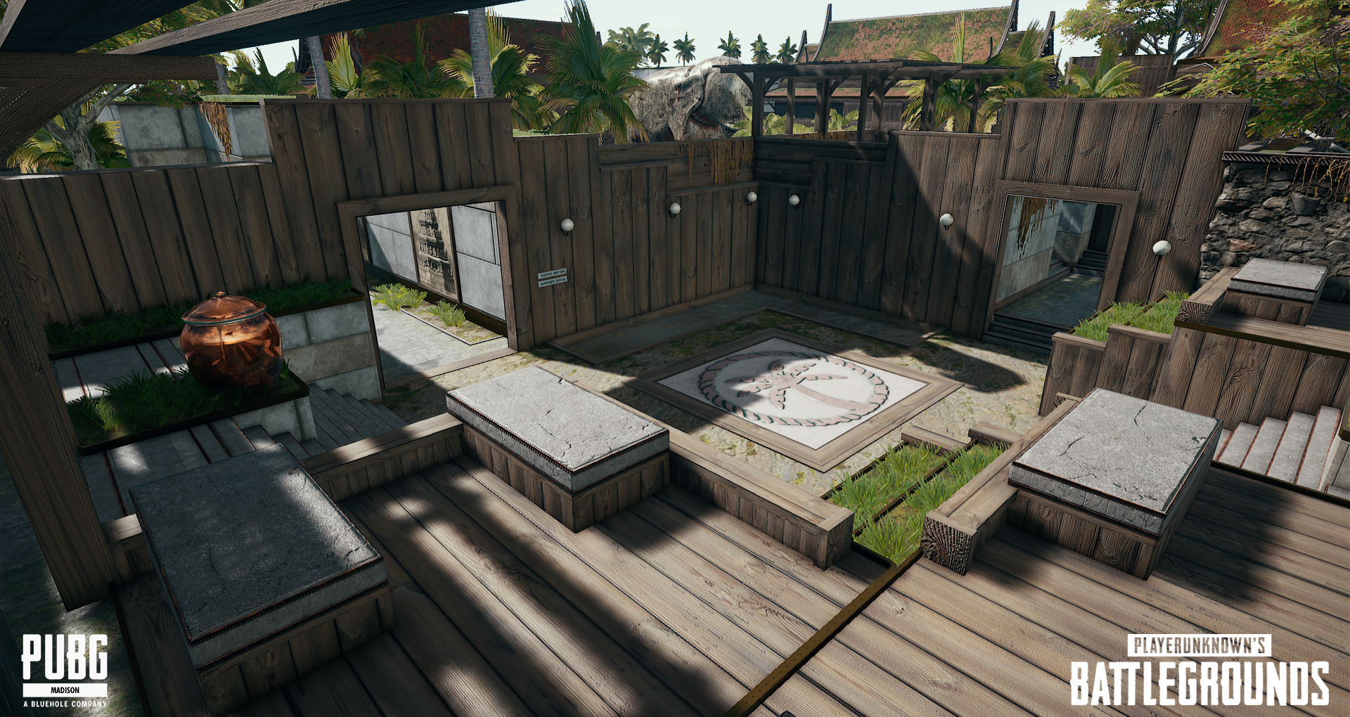 In-game scene from PUBG Battlegrounds showing a wooden rooftop terrace with benches, greenery, and a large emblem in the center.