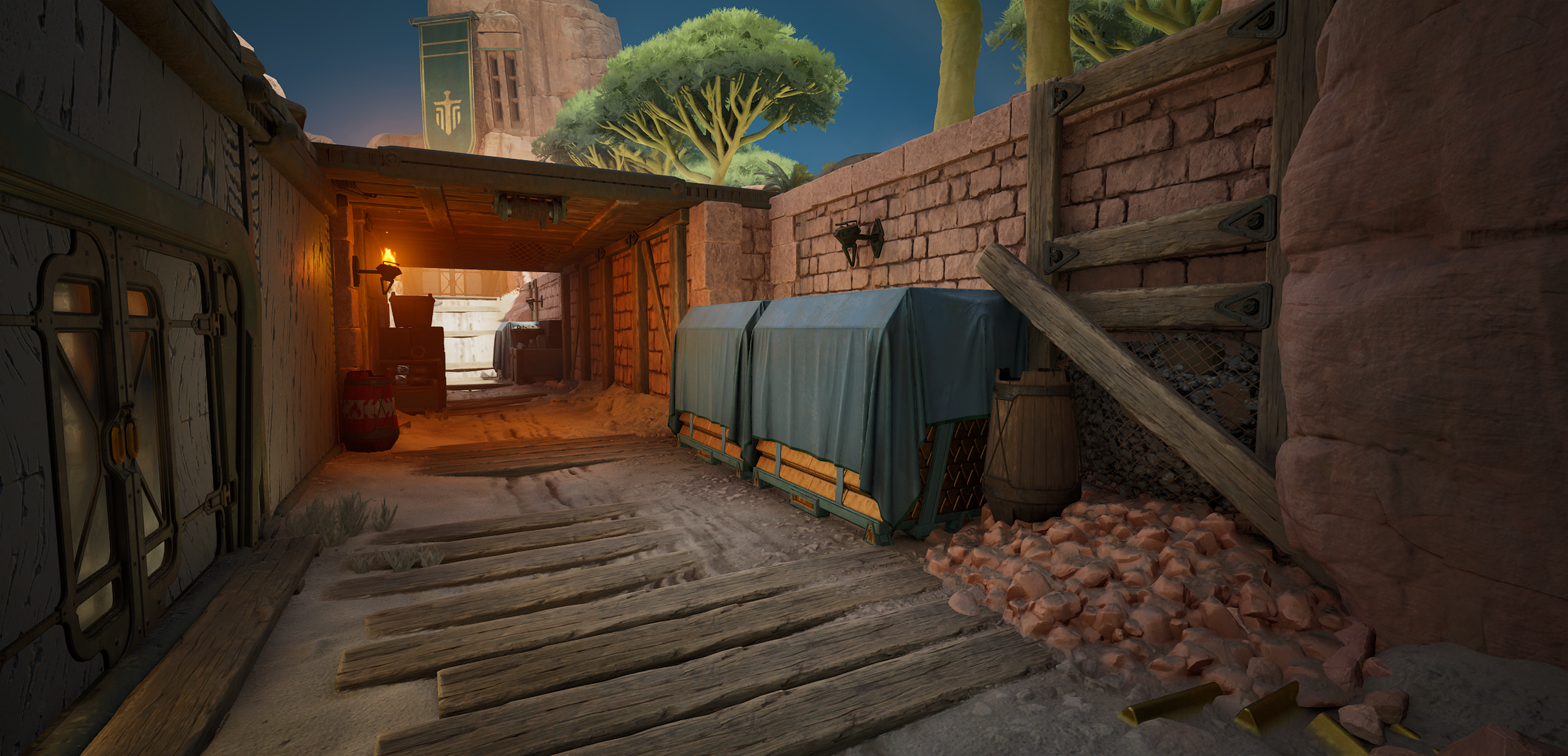 A dirt alleyway in a desert environment with wooden planks on the ground, stone walls, and a wooden staircase leading up. There are covered objects, a barrel, and a lit torch on the wall. In the background, trees and a building with a banner are visi