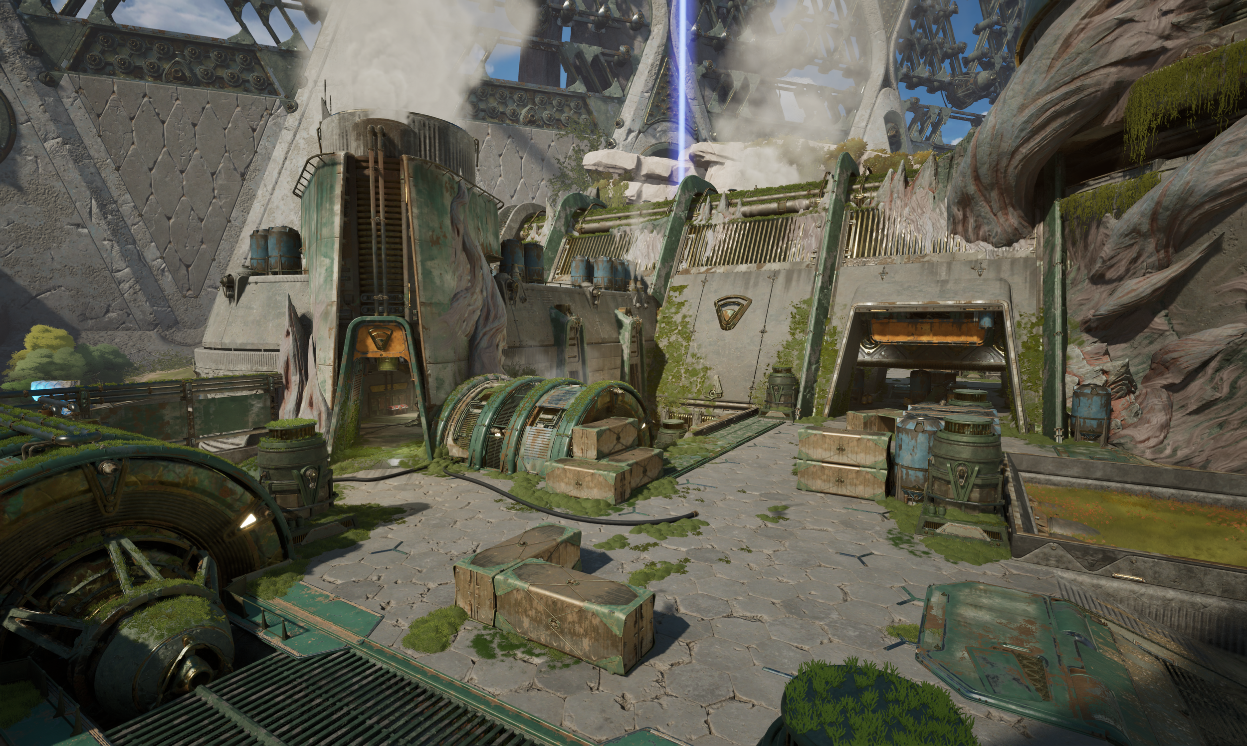 Futuristic industrial outpost with weathered green metal structures, crates, barrels, smoke, and moss overgrowth amidst rocky terrain and cloudy sky.