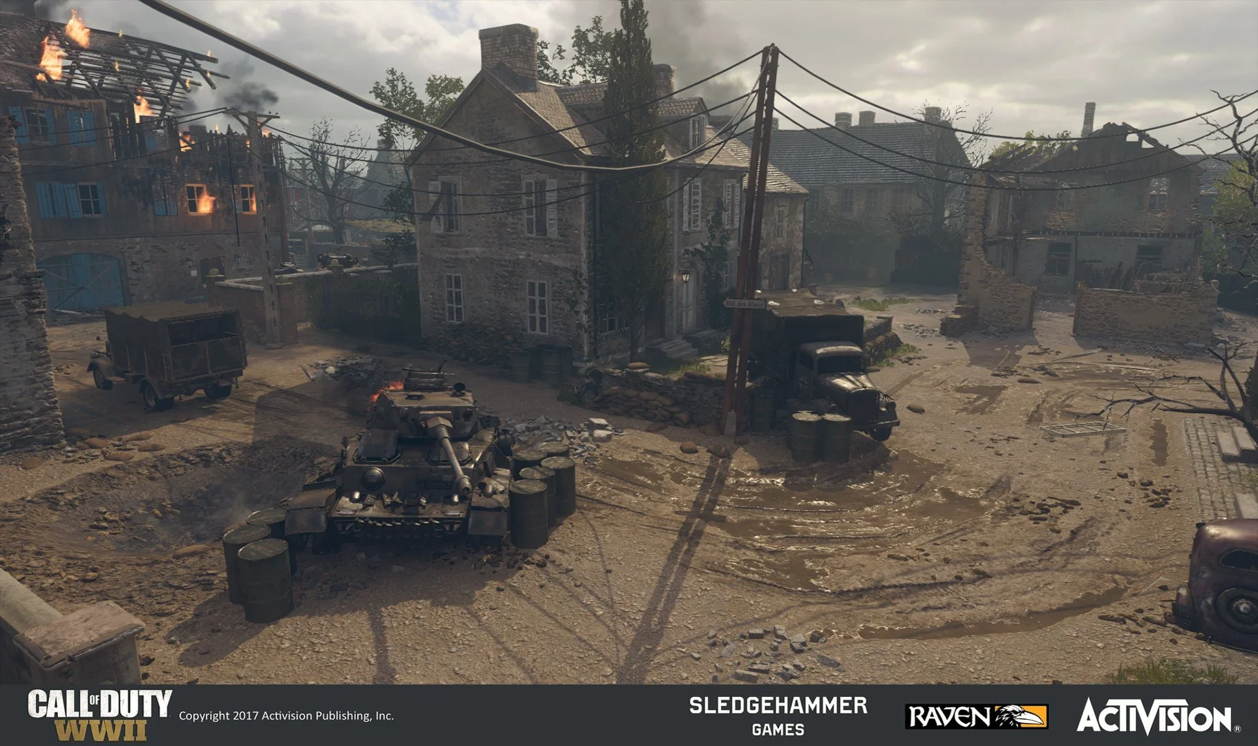 A war-torn village street with damaged buildings, a burning house on the left, a tank in the foreground, and military trucks, under a cloudy sky.