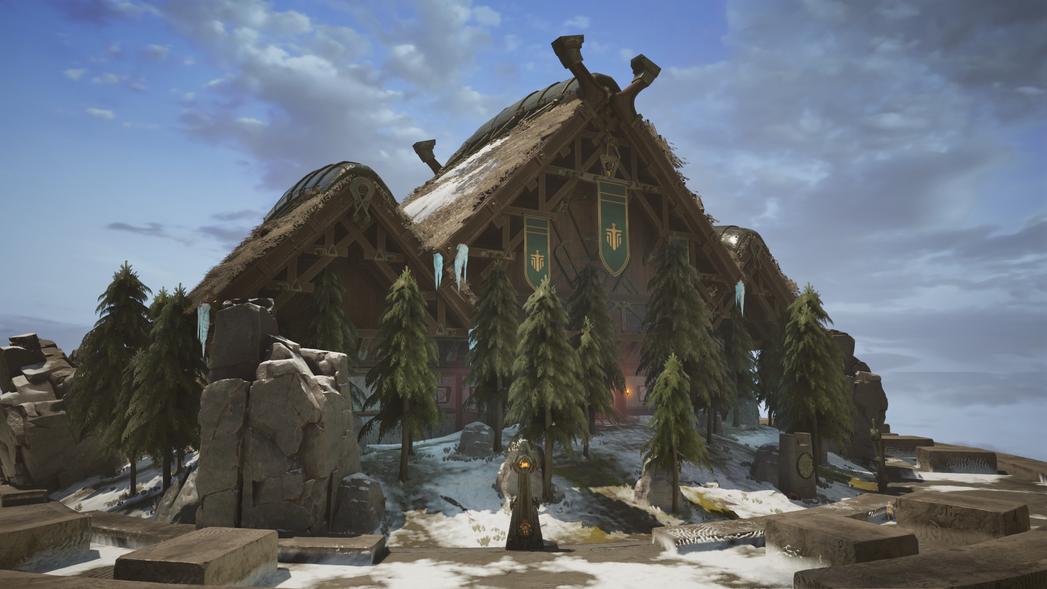 A large, wooden, A-frame building with banners hanging from the front, surrounded by snow and pine trees on a rocky landscape under a cloudy sky.