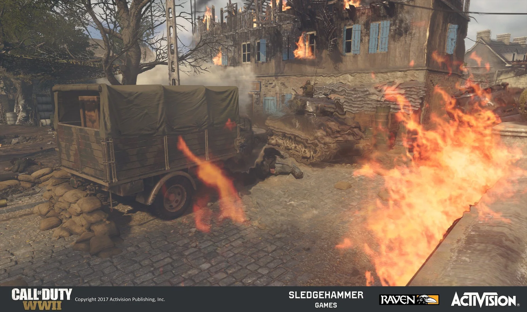 Screenshot from the video game Call of Duty WWII showing a wartime scene with a burning building, a military truck surrounded by sandbags, and soldiers in combat amidst flames and smoke.