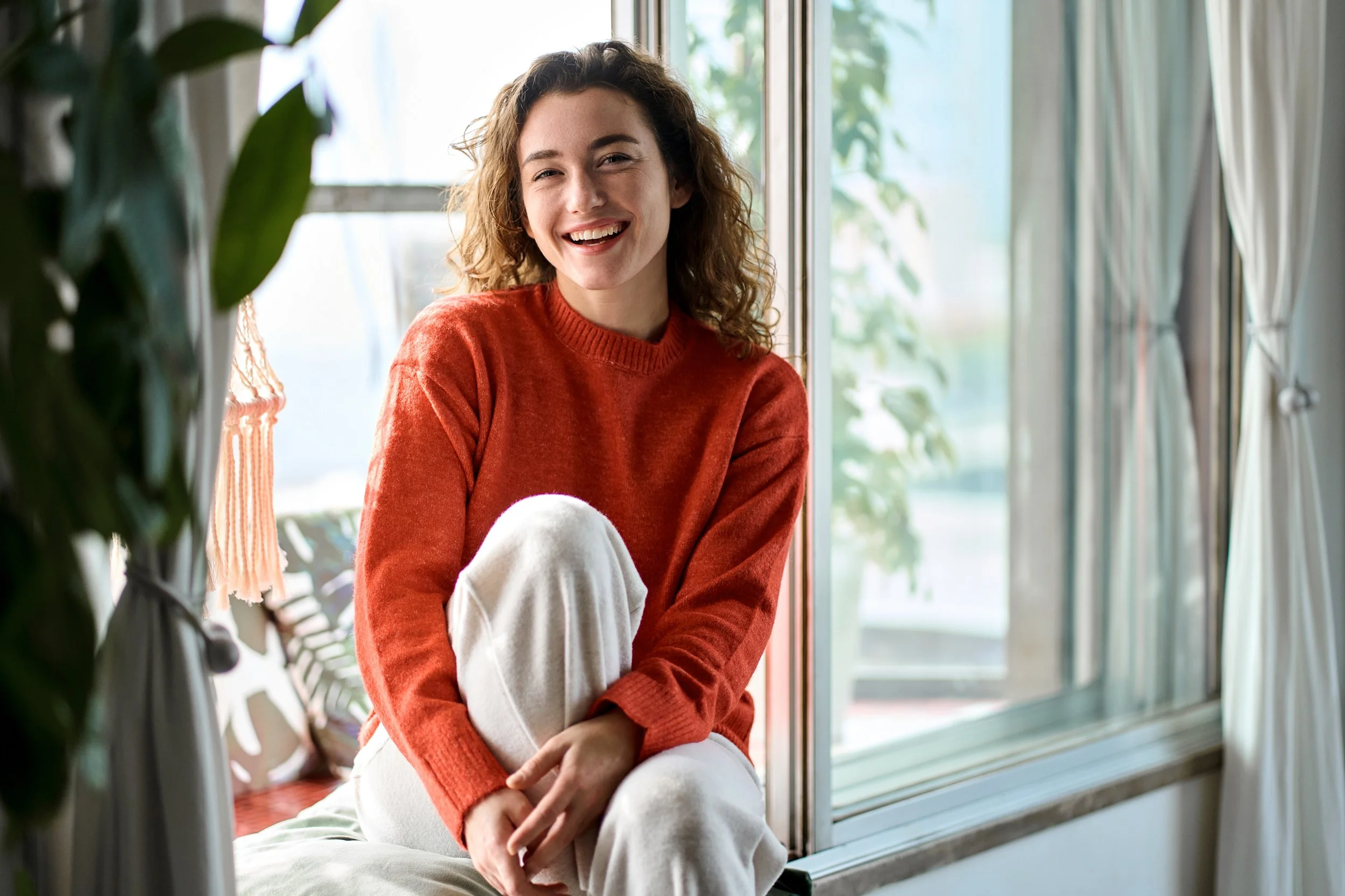 woman sitting by window in red sweater smiling