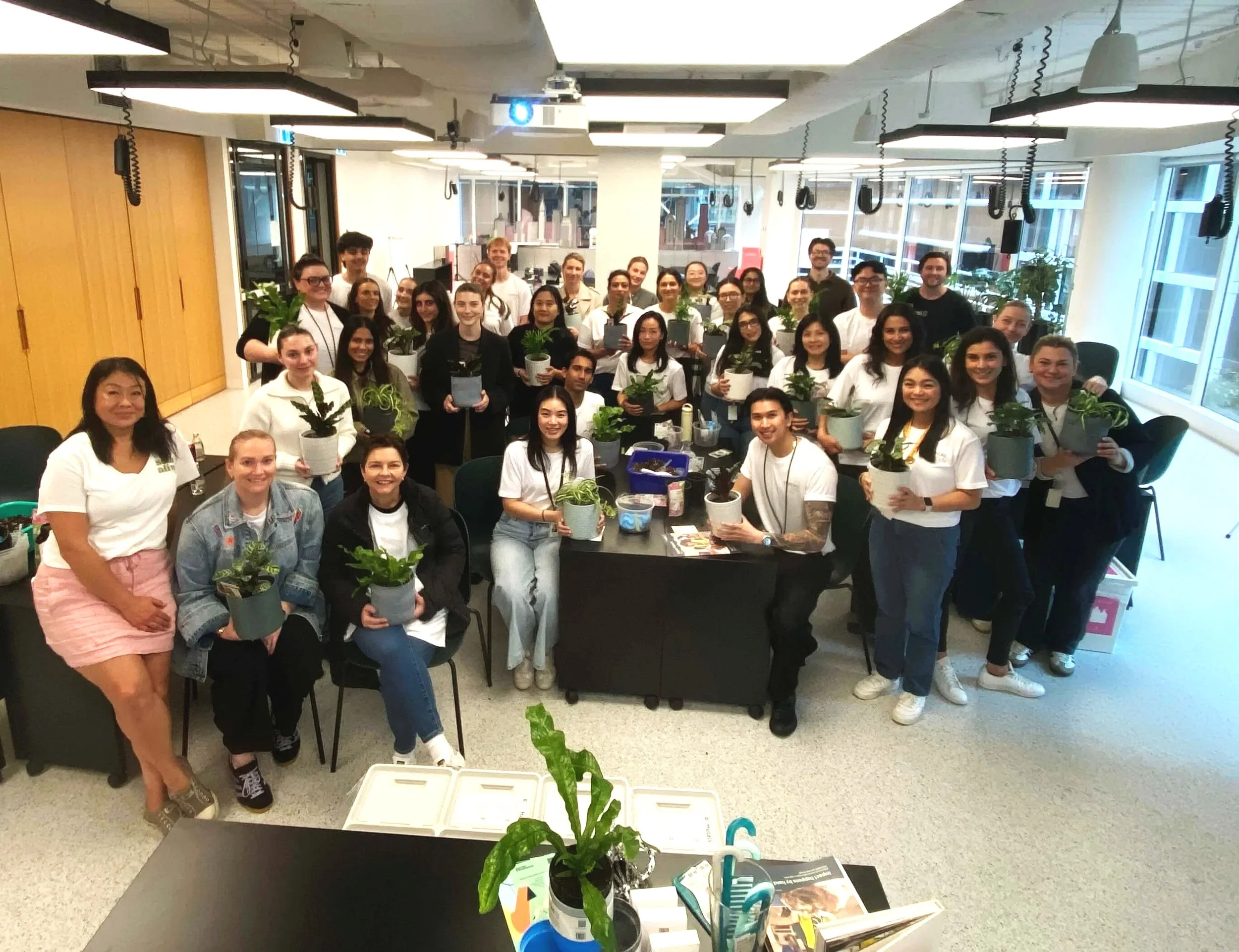 Group of people in an indoor space, holding potted plants, some smiling at the camera.