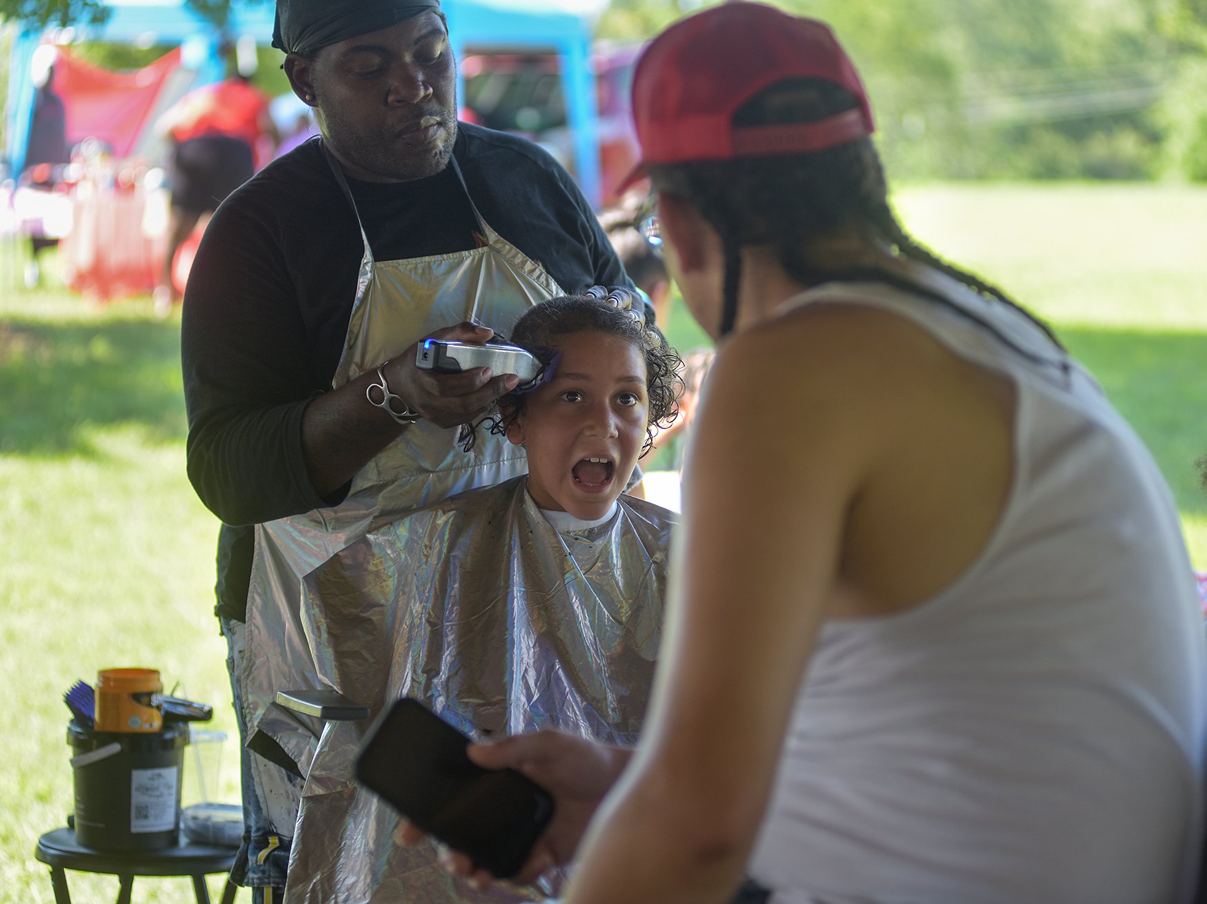 King Parker, 7, has his long summer curls shaved off by barber Roy Lovelady, left, while his dad George Parker watches on Aug. 20 at Albert-Oakland Park.