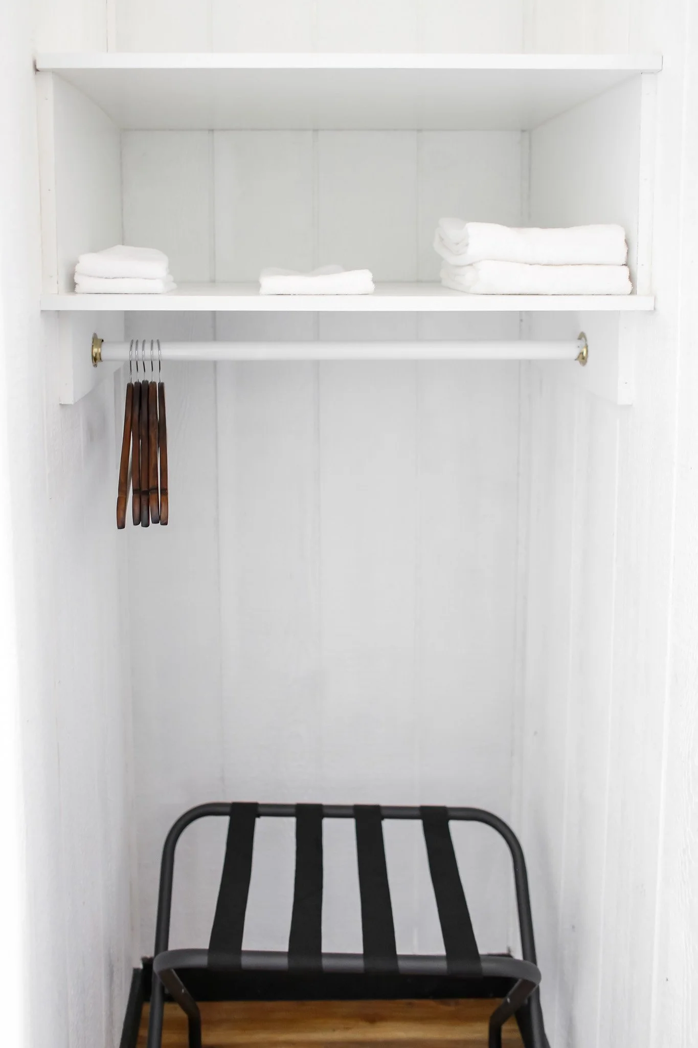 Simple white closet with towels, hangers, and luggage rack.