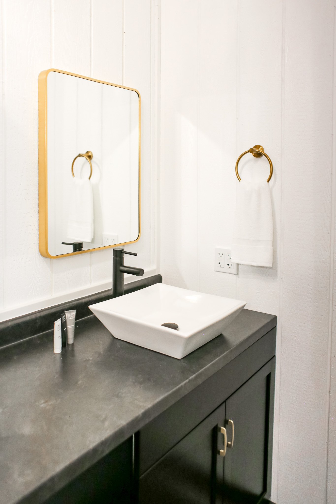 Modern bathroom with rectangular mirror, vessel sink, black faucet, and white towel on gold ring