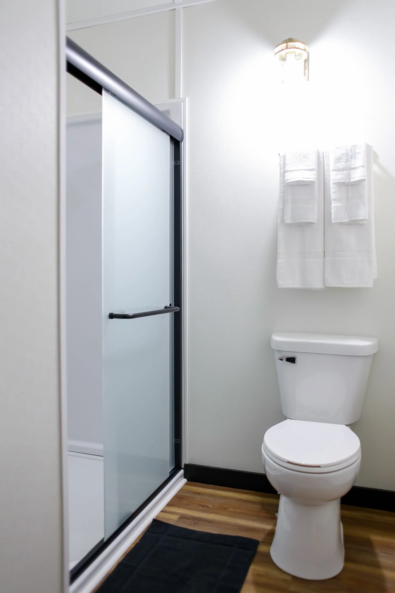 Modern bathroom with toilet, glass shower door, towels, and light fixture.
