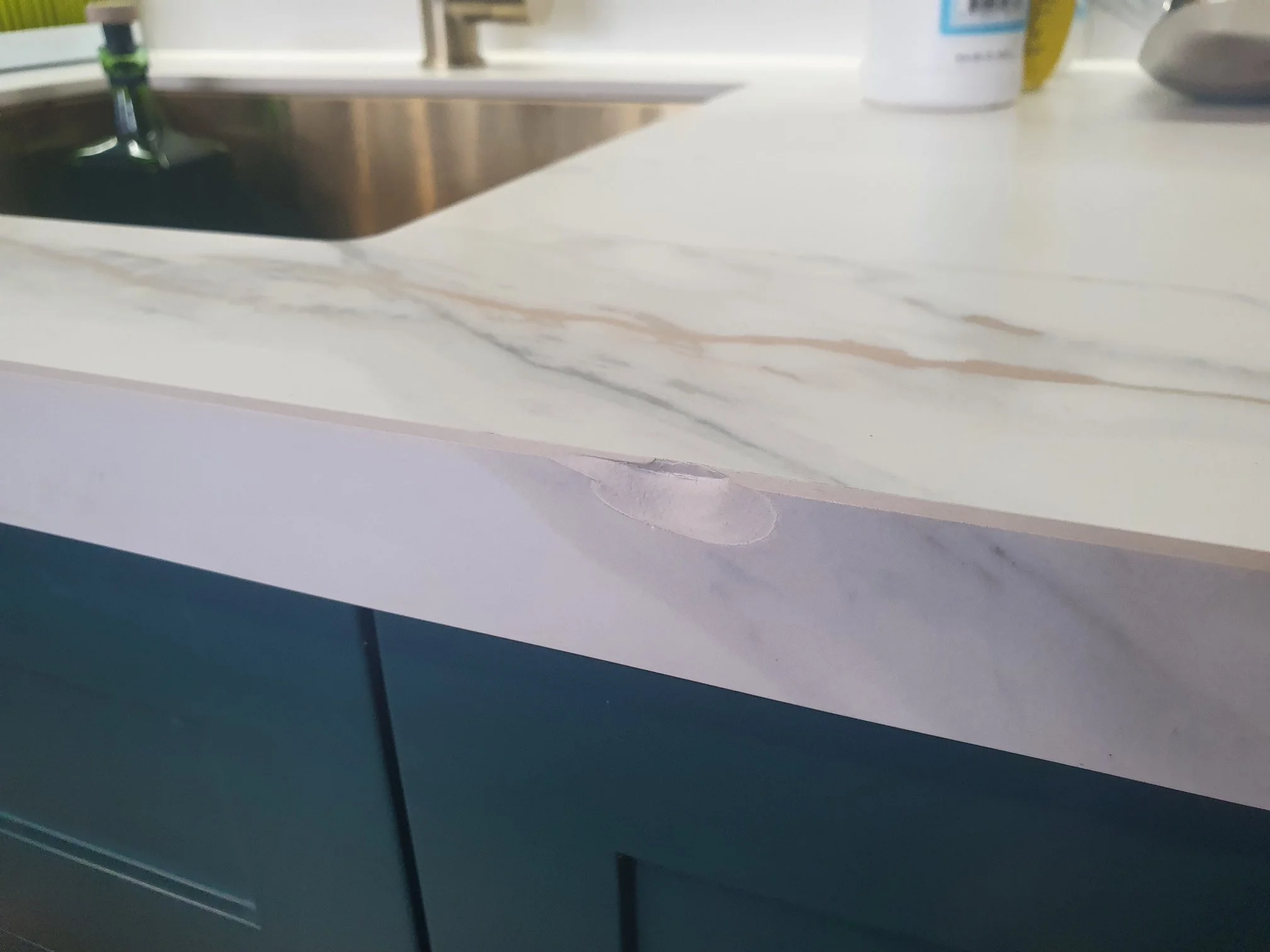Close-up of a kitchen countertop with a visible tear or dent on the edge, showing a marble or quartz surface.