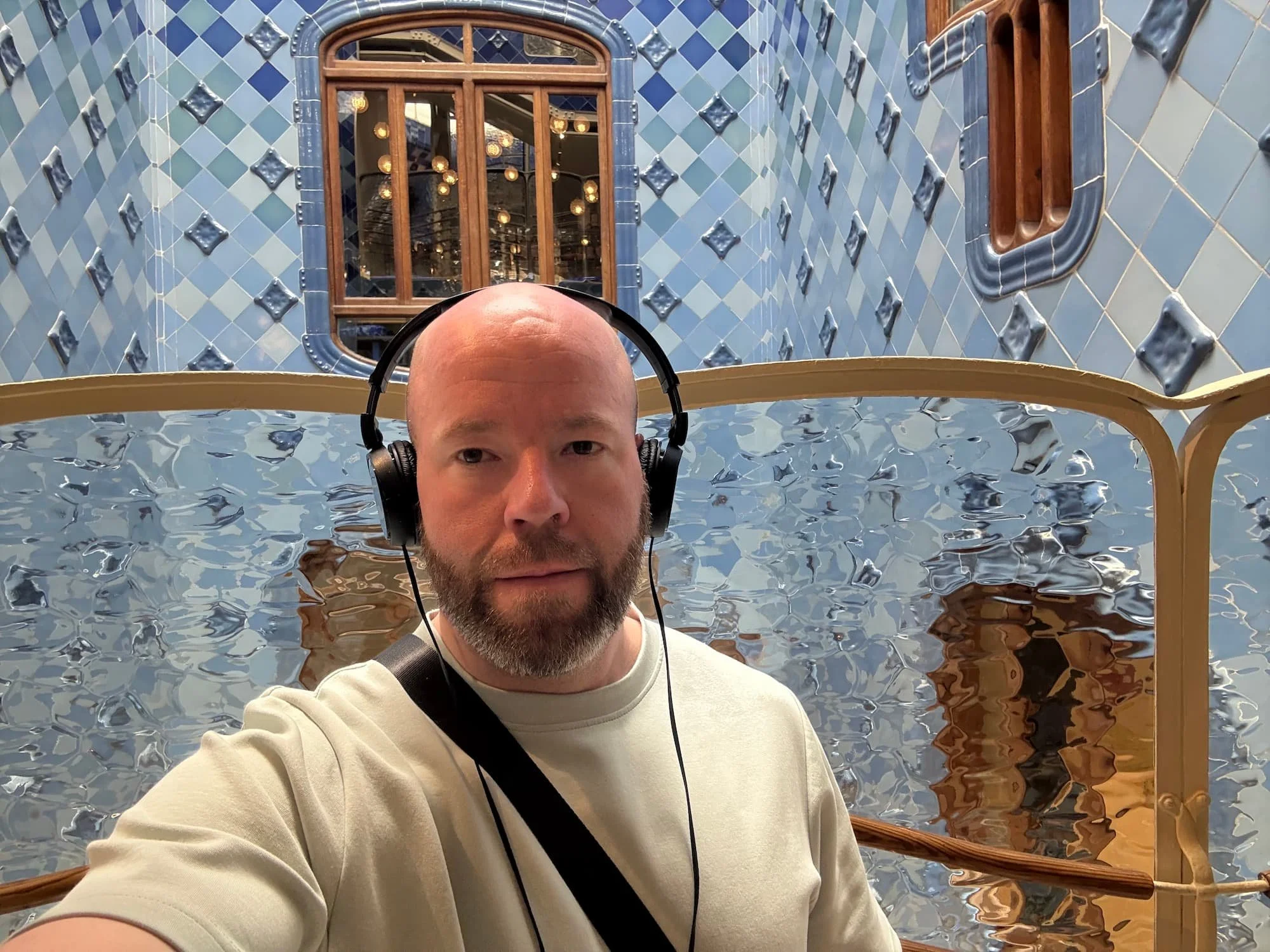Tom Henty wearing headphones inside Casa Batlló's blue-tiled light well while using the immersive audio guide experience.