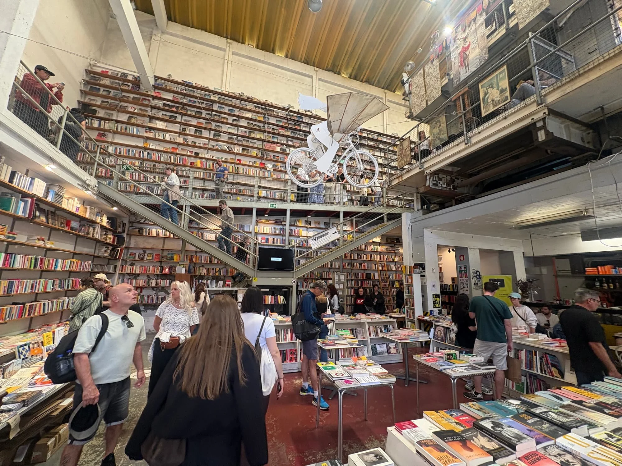 Interior of Ler Devagar bookshop at LX Factory in Lisbon, featuring towering bookshelves, industrial architecture and the famous suspended flying bicycle sculpture.