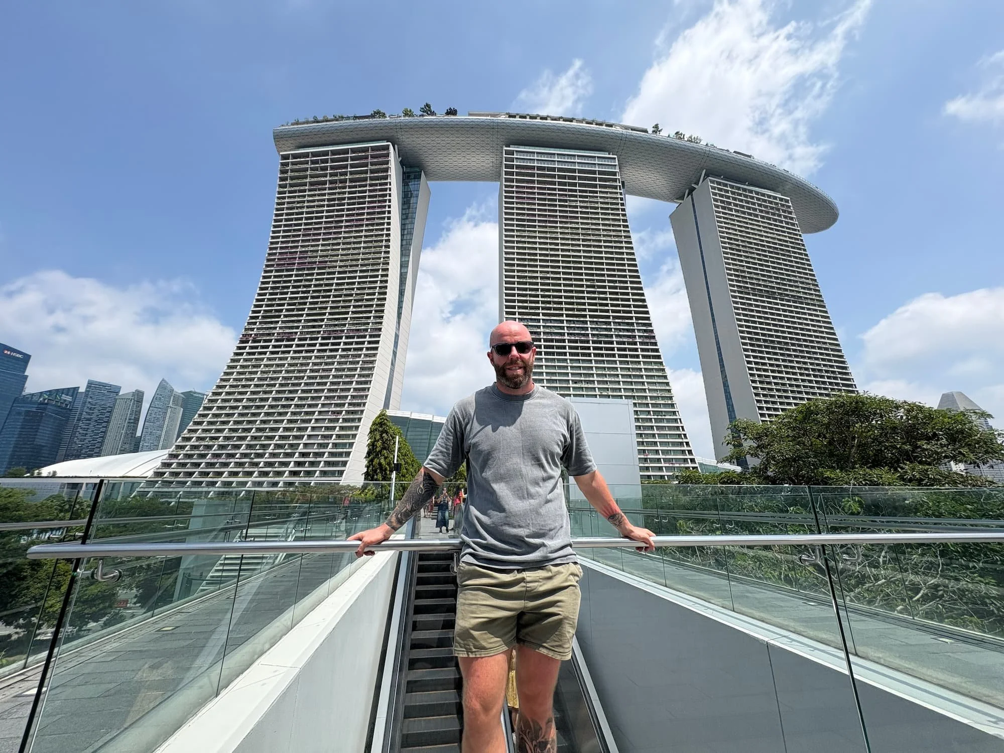 Tom Henty standing on a pedestrian walkway with views of Marina Bay Sands and Singapore’s modern skyline behind.