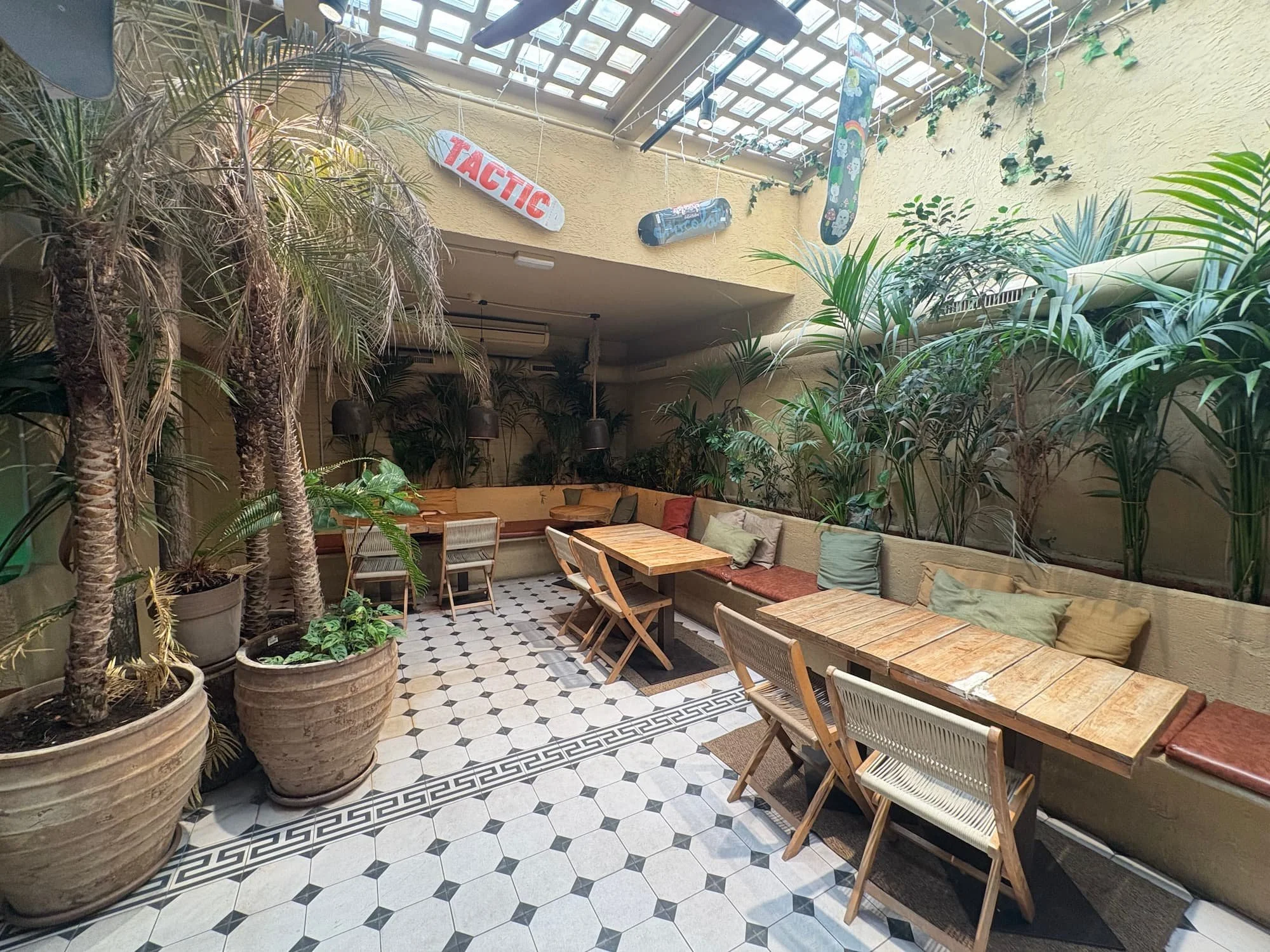 Indoor seating area at Surf House Barcelona, featuring tropical plants, wooden tables and a relaxed café atmosphere near Barceloneta Beach.