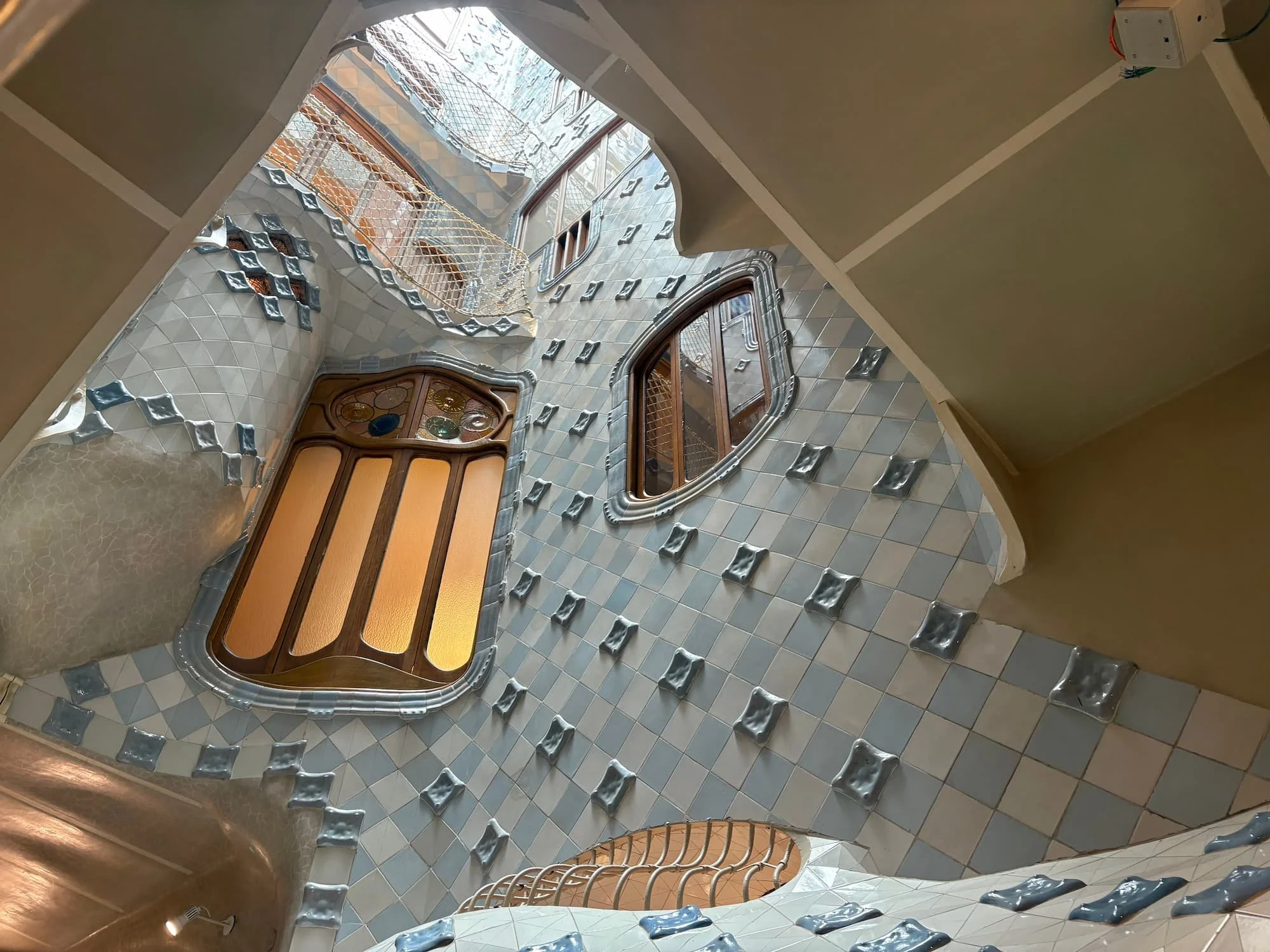 Looking up through Casa Batlló's central light well, featuring curved balconies, blue gradient tiles and organic windows designed by Antoni Gaudí.