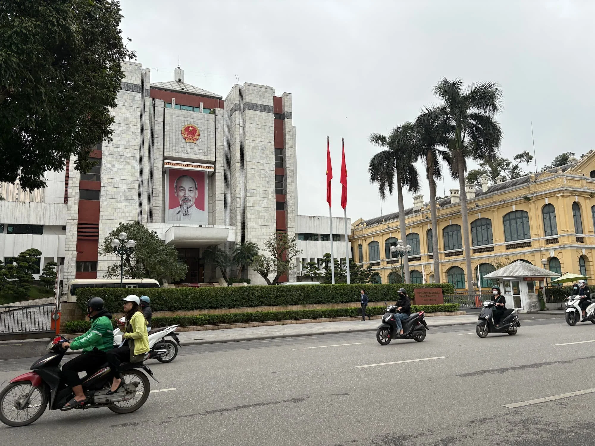 Scooters riding past a building in Hanoi with Ho Chi Minh's face on
