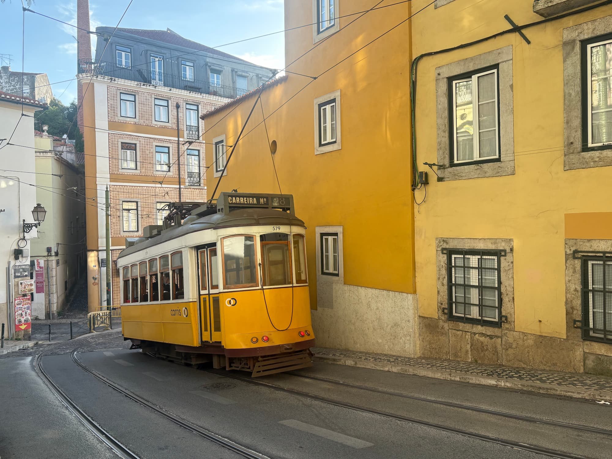 Traditional yellow Tram 28 travelling through the colourful streets of Lisbon, Portugal, surrounded by historic buildings in the Alfama district