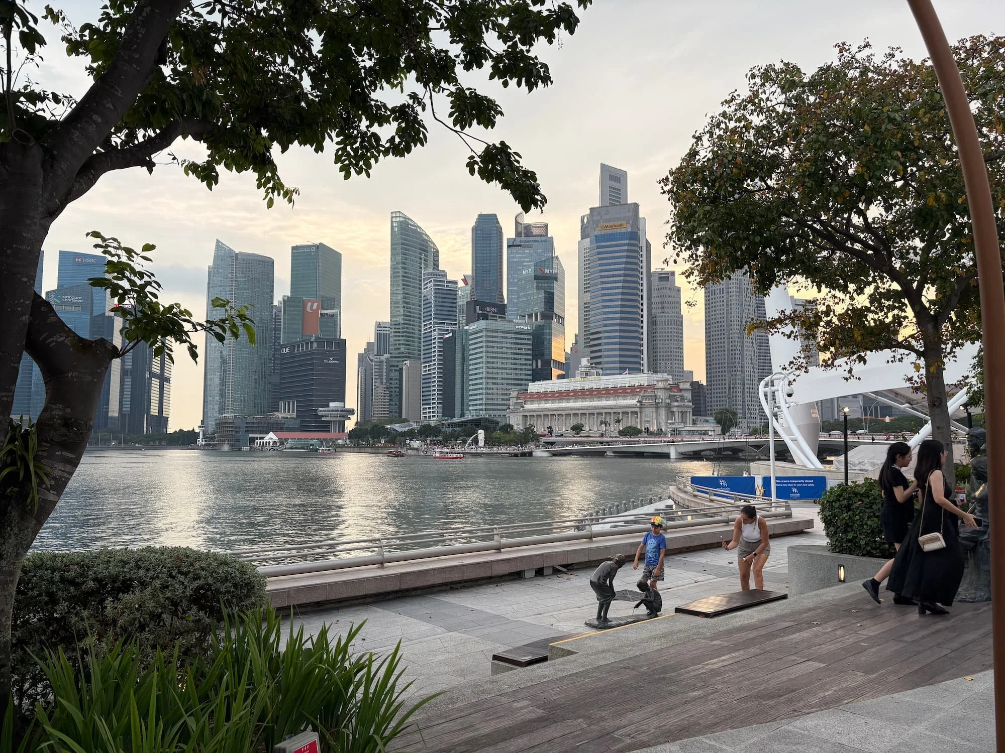 Singapore skyline viewed from Marina Bay promenade, showing modern skyscrapers, waterfront walkways, and people exploring the city on foot.