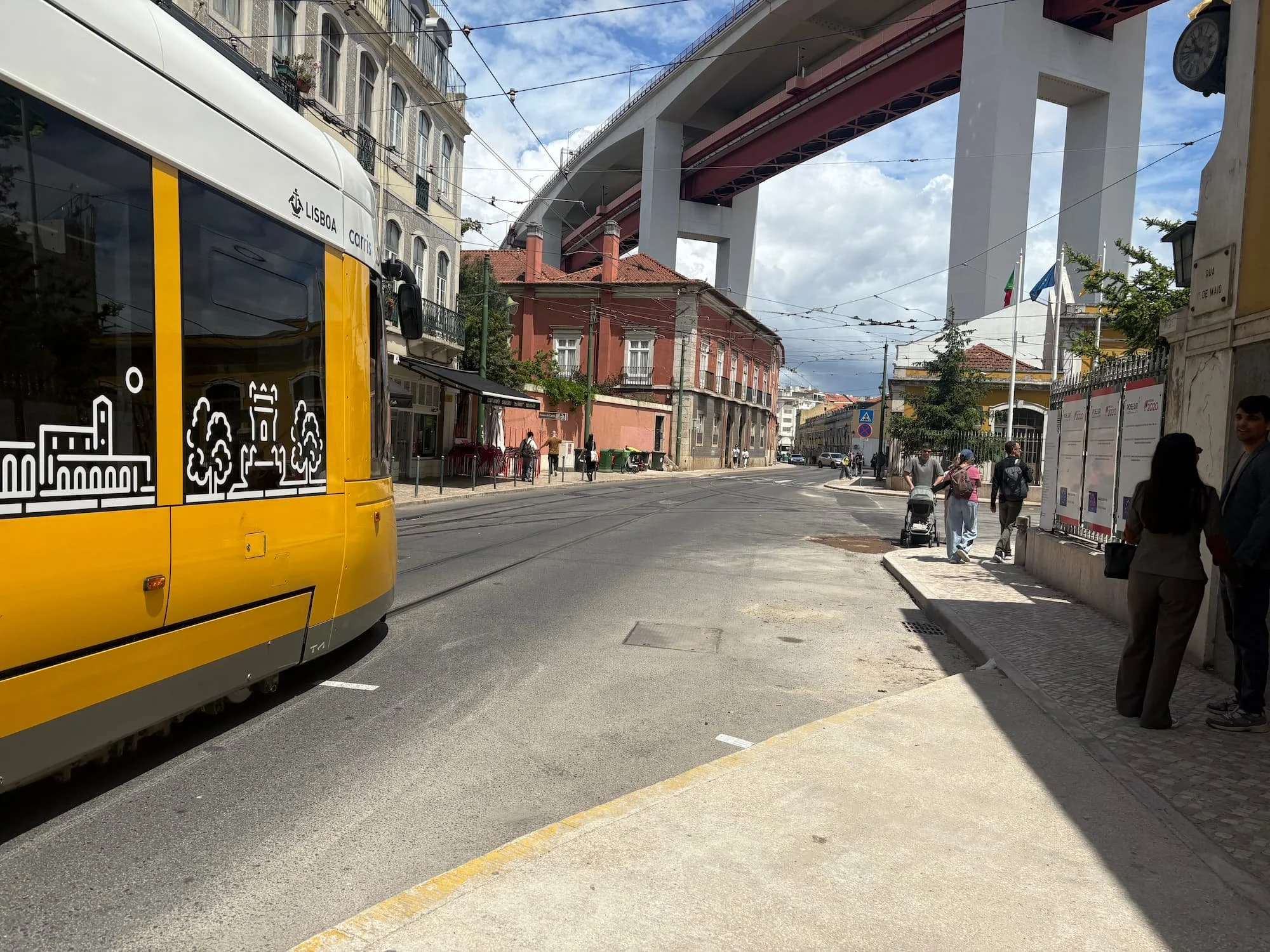 Modern yellow Lisbon tram travelling beneath the 25 de Abril Bridge in Portugal, connecting different parts of the city.