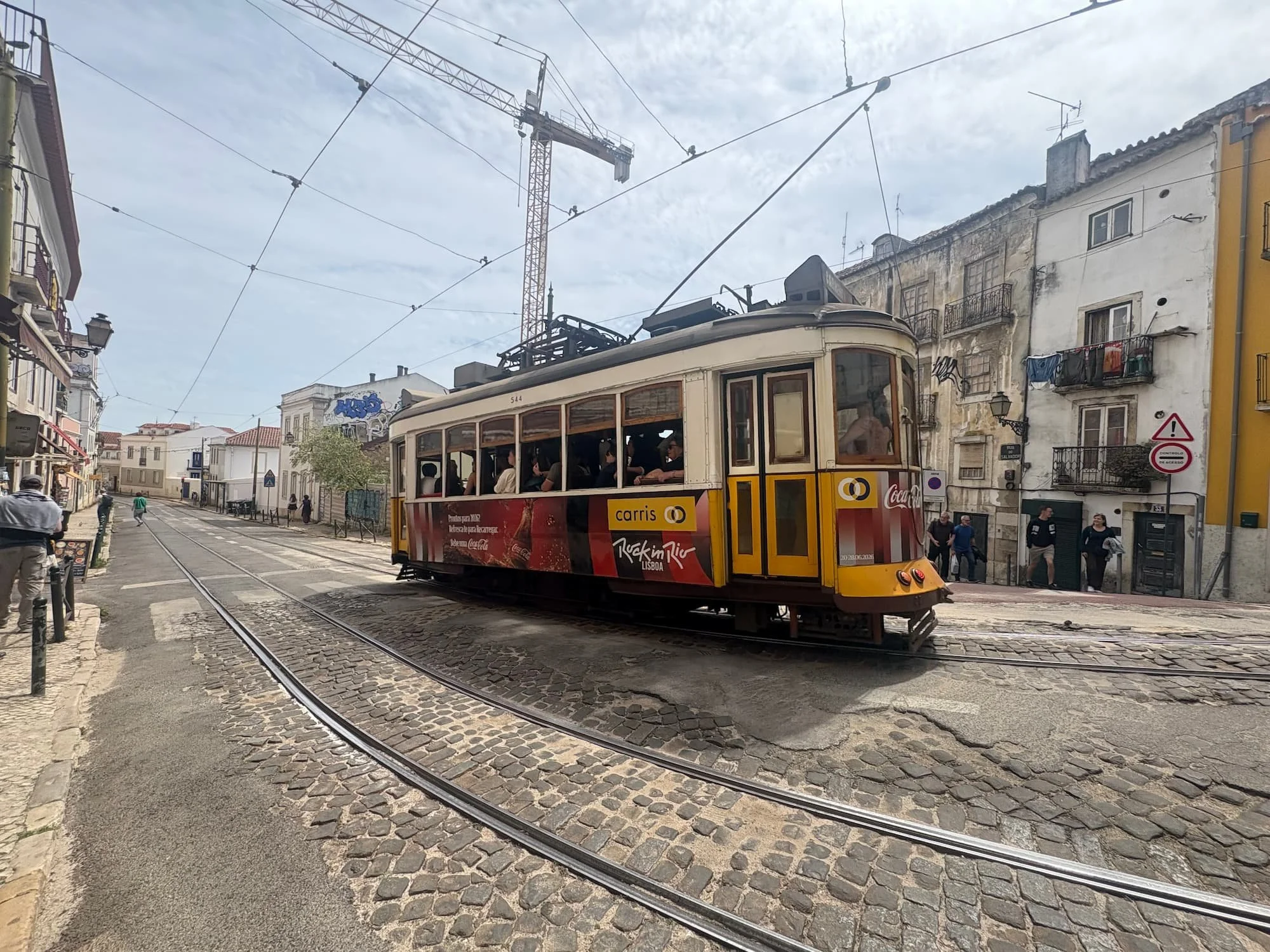 Traditional yellow tram travelling through the cobbled streets of Lisbon, Portugal, surrounded by historic buildings and overhead tram lines.