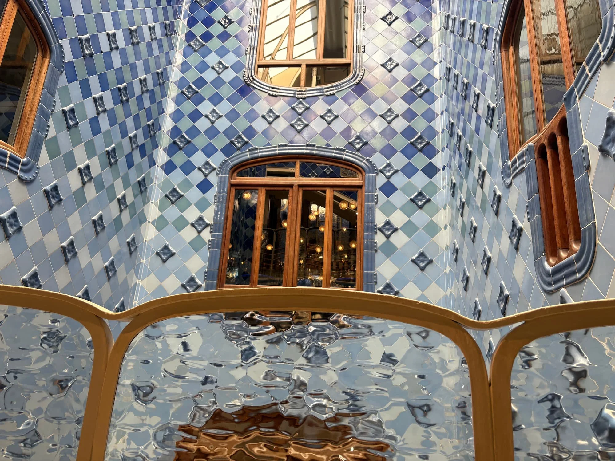 Blue-tiled light well inside Casa Batlló featuring Gaudí's gradient ceramic tiles, wooden windows and flowing organic design.