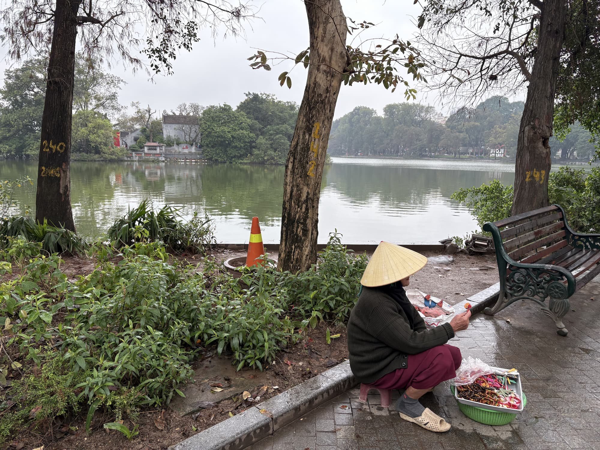 Local souvenir seller wearing a straw hat at Hoàn Kiếm Lake in Hanoi in Vietnam
