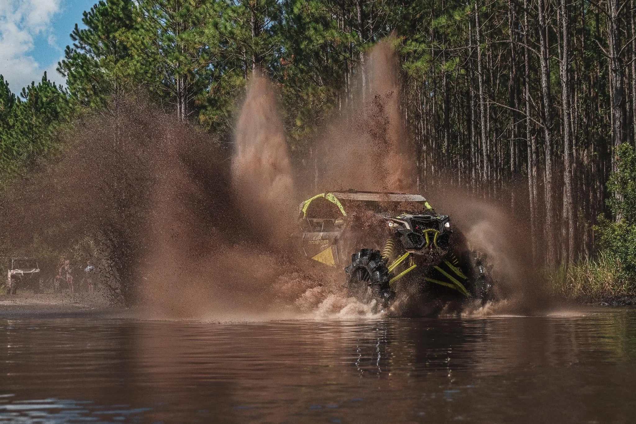A side-by-side blowing through a water hole on a wooded trail.