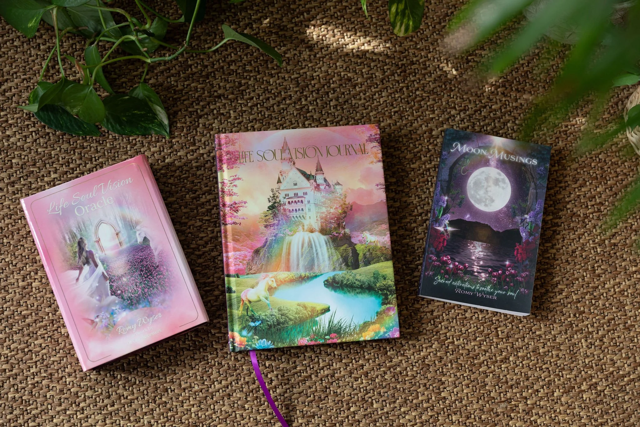 Romy Wyser's Life Soul Vision Oracle, Life Soul Vision Journal and Moon Musings journal displayed on a woven mat surrounded by greenery.